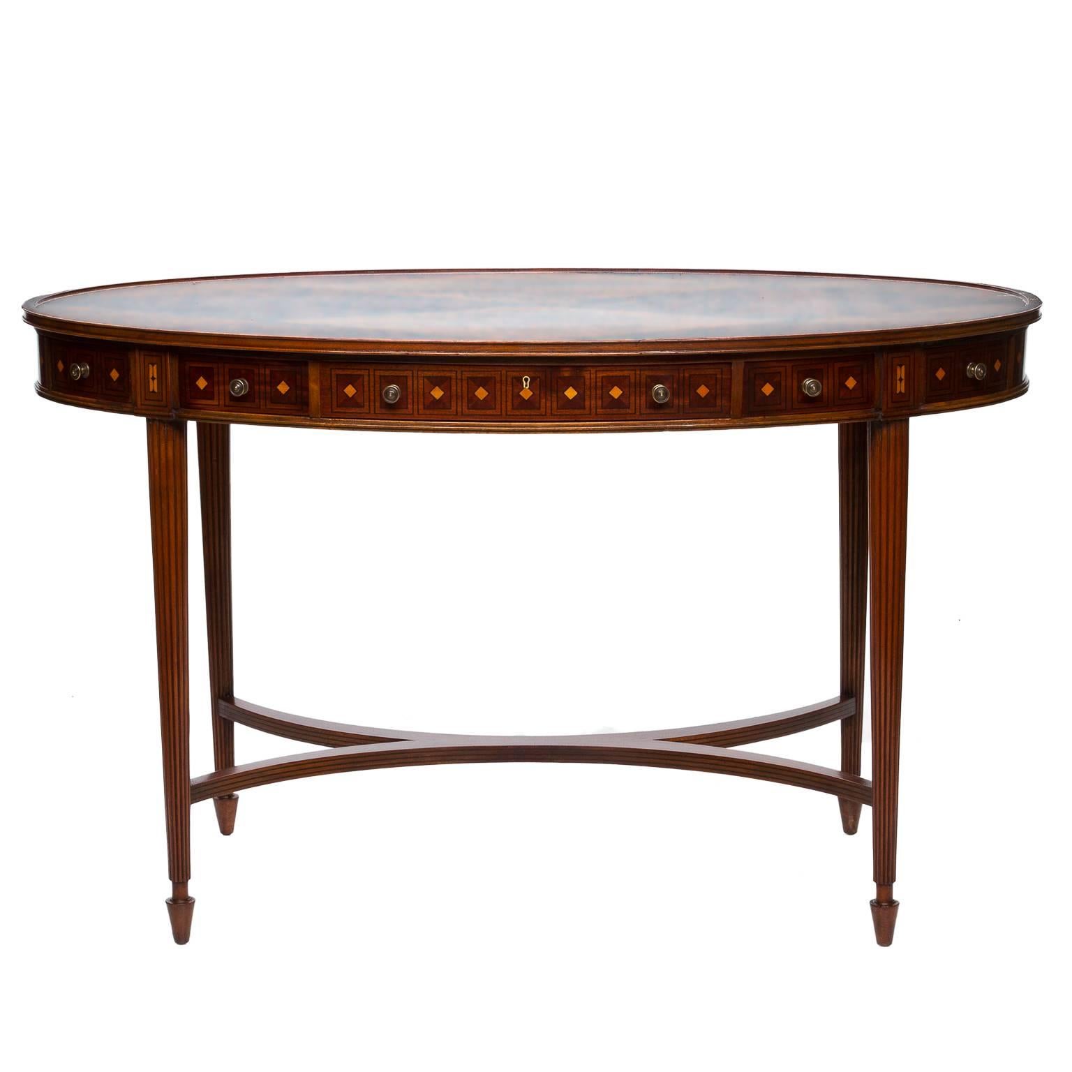 A vintage English inlaid oval writing desk. Fine inlay work was performed on this desk! Functional drawers on one side. A reeded tapered leg leading down to turned feet. An X-stretcher. Beautiful diamond shaped patterned veneered top. Mahogany cuts