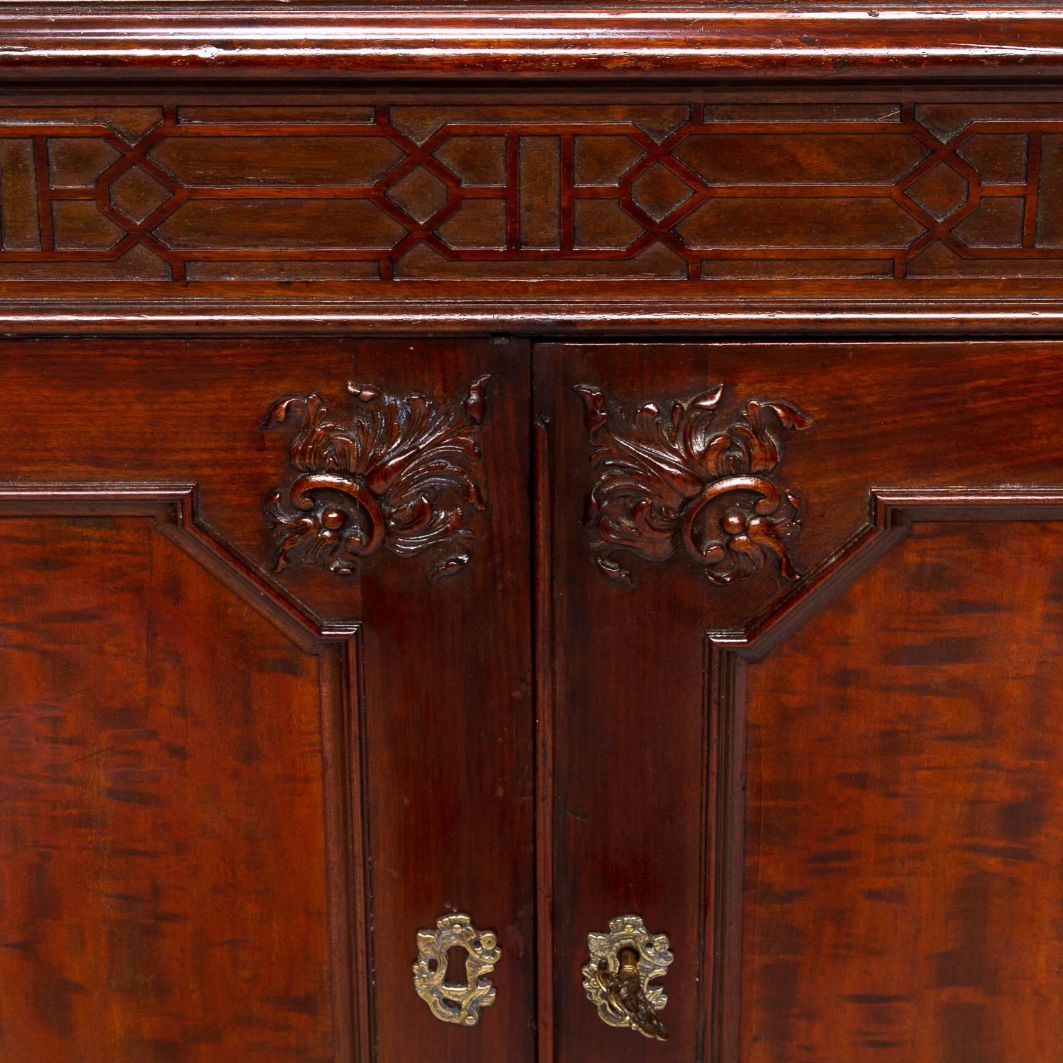 A fine solid mahogany cabinet in the Chippendale style. Wonderful rich color and fine carved details. Excellent craftsmanship to blind fretwork which gives it overall design. Resting on for tapered legs. Ribbon and flame cuts of wood. Two doors open
