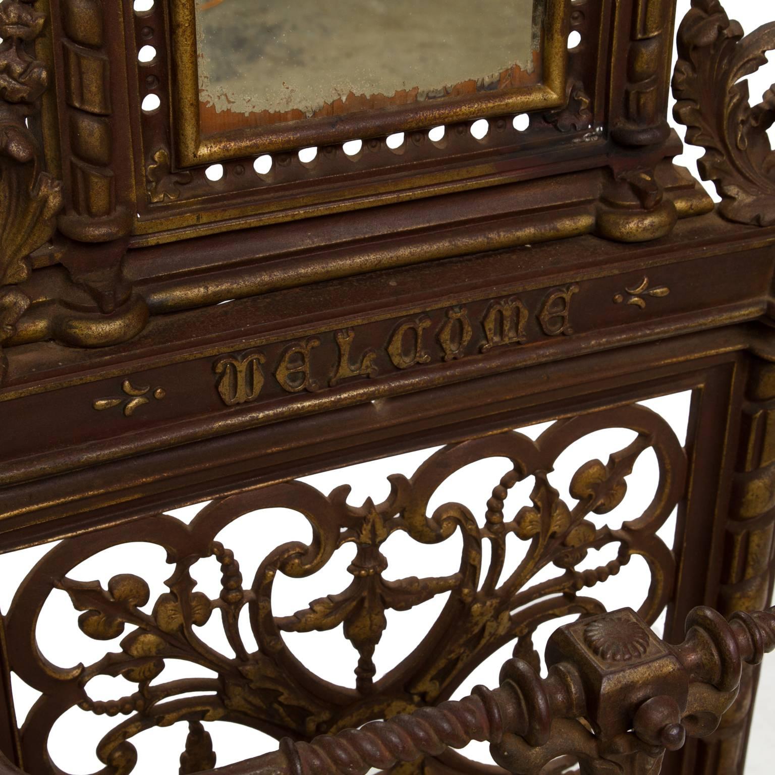 A handsome 19th century cast iron hall tree from England. There are six hooks surrounding an arched mirror. Wonderful scroll details including an lions mask, floral swags and the word welcome below the mirror. Great color and sturdy. One hook has