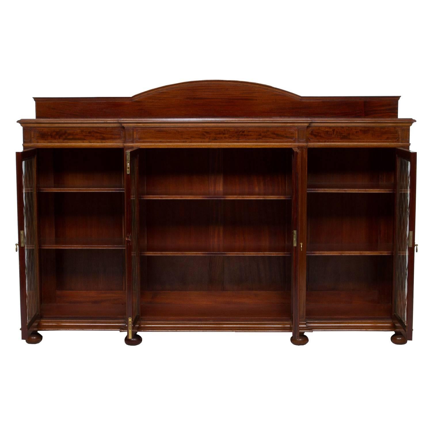 An impressive English mahogany credenza bookcase with a breakfront. There are four doors and each with glass and a brass mesh in a diamond shaped pattern. Fine French polish over carefully chosen figured mahogany. Resting on bun feet. The breakfront