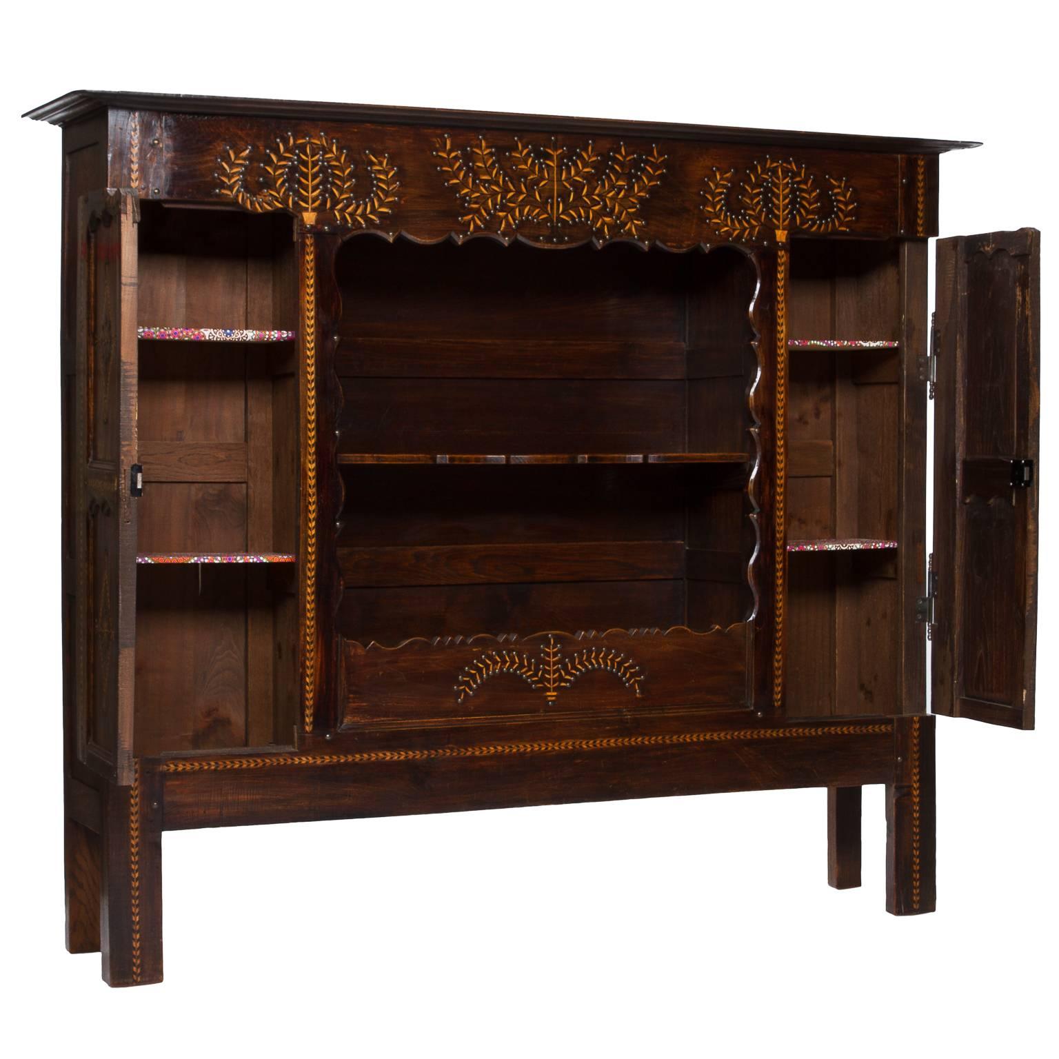 A very unique piece in the style of French Provincial which is heavily inlaid and highlighted with aged brass tacks. Originally a bed front it was converted long ago to a beautiful bookcase. Featuring two ample locking side cabinets, metal hinges,