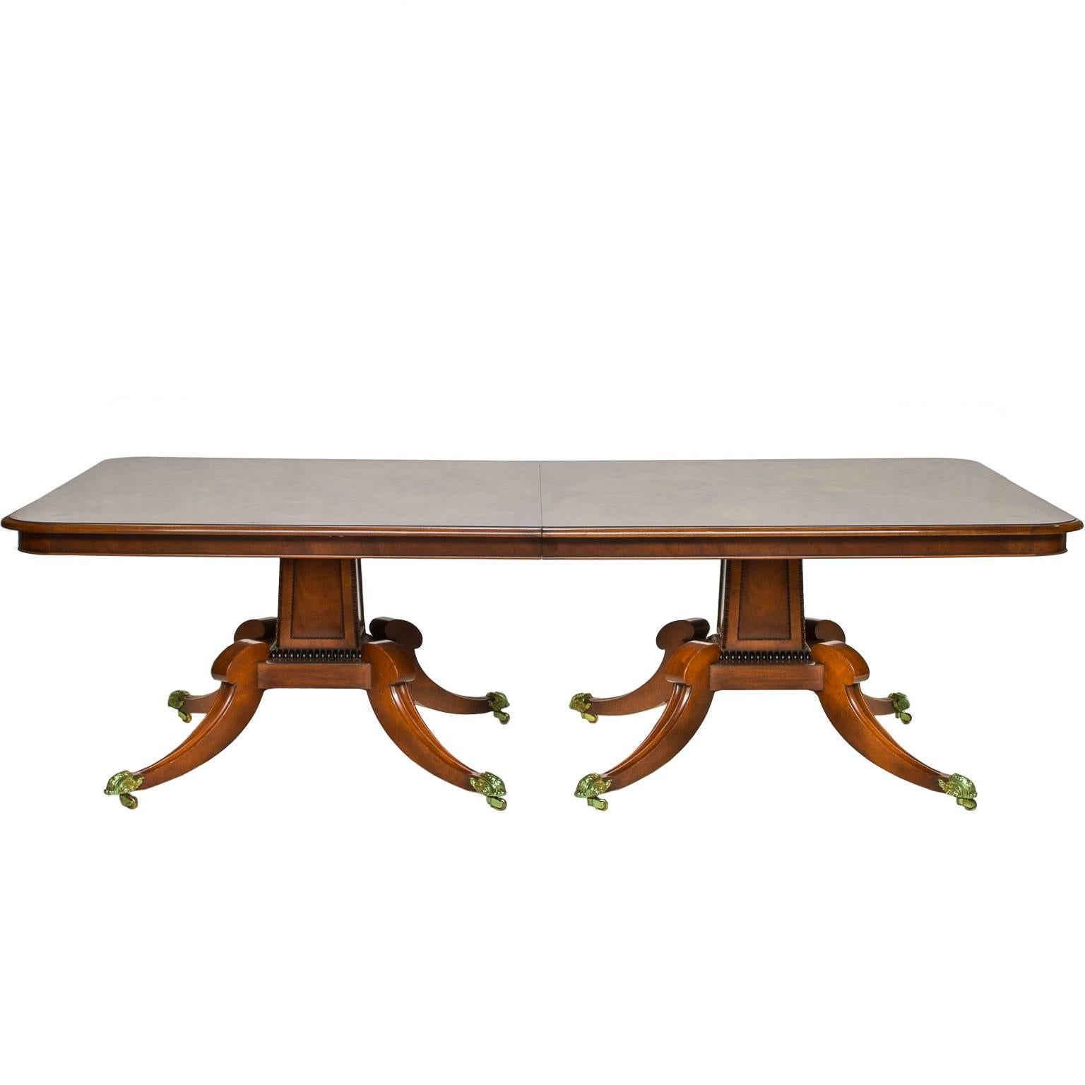 An English mahogany two pedestal, two-leaf dining table in the Regency style. This table has a beautiful top. Choice cuts of mahogany with multiple color tones. Nice figuring to the grain. A string inlaid of ebony. A bullnose edging and apron below.