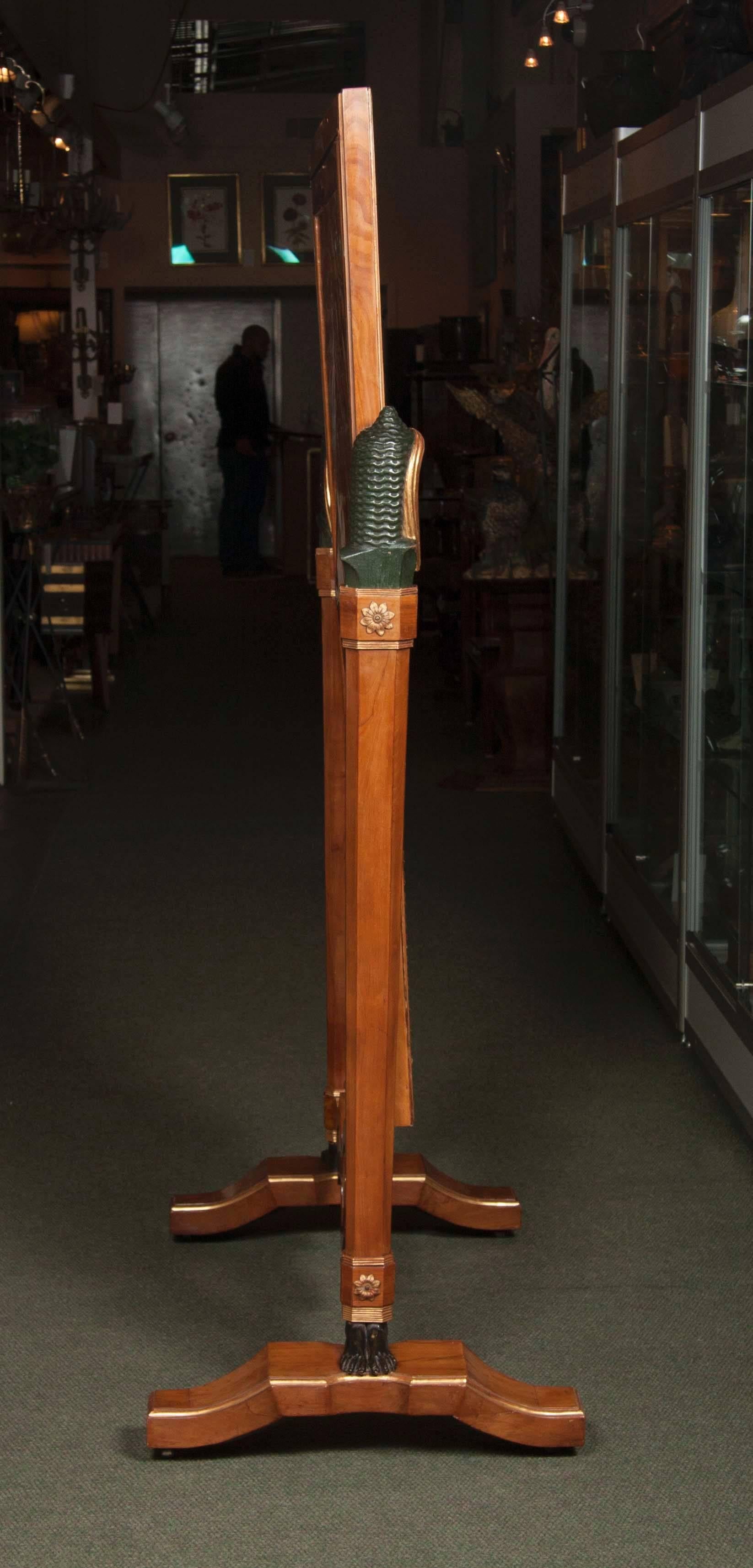 An Italian cherrywood, Egyptian Revival cheval glass mirror with gilding and hand carved appliques.  The columns are adorned with carved standing ebonized feet upon a sculptural base/  The top of the capitols are adorned with carved and gilt