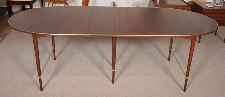 A Walnut and brass drop-leaf dining table with four individual leaves. Paul McCobb Connoisseur Collection - H. Sachs & Sons. Signed.

Four leaves are each 11