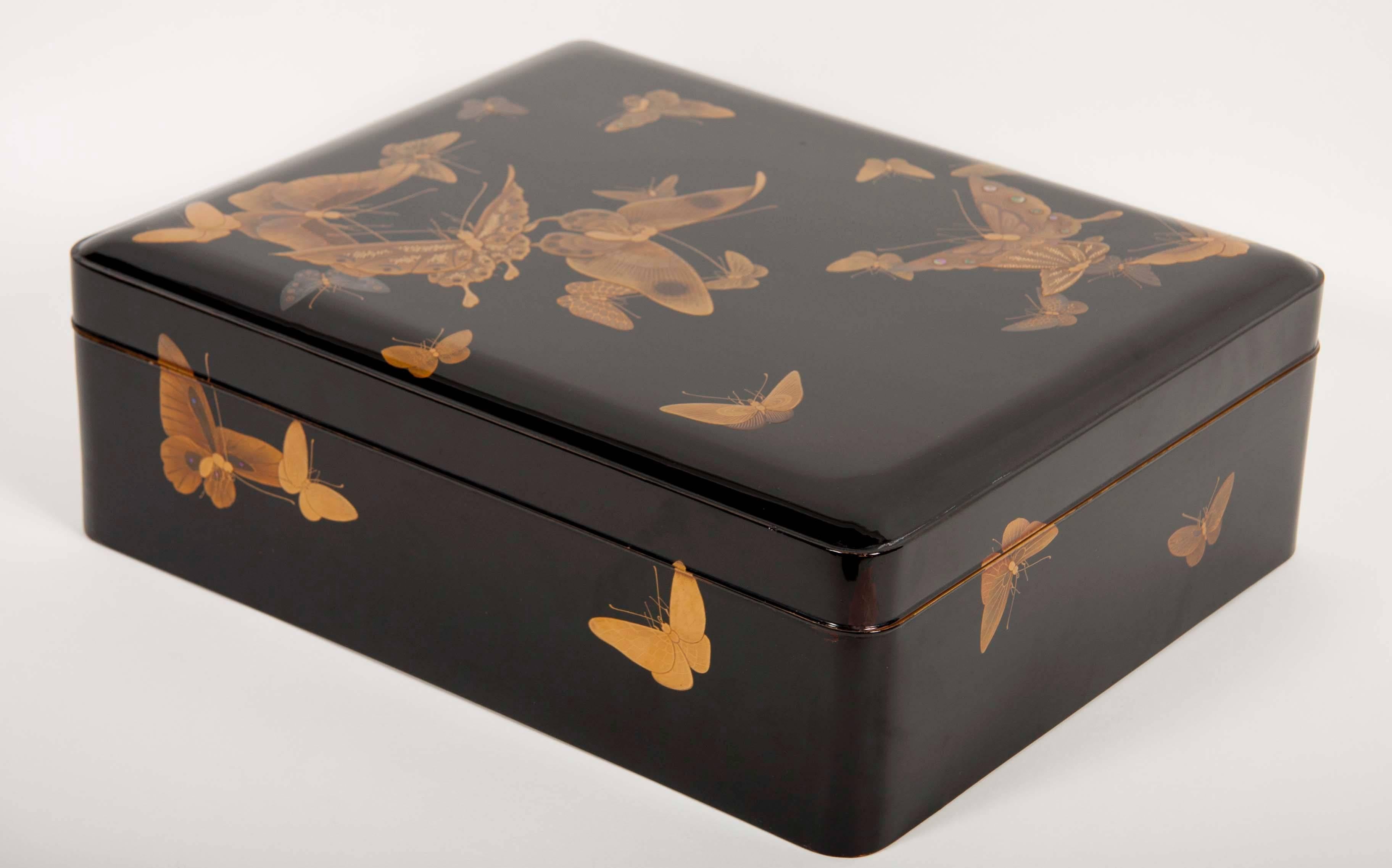 A large early 20th century Japanese Ryoshibako (document) box of black lacquer with rounded corners beautifully decorated with gold butterflies. The interior of the lid having additional decoration in gold set on a dark red background of water with