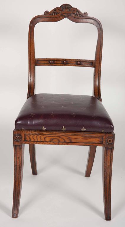 A set of eleven English Victorian oak dining chairs comprising two armchairs and nine side chairs. Chairs have leather seats with gold tooling. The measurements of the armchairs are: 34.5 H x 22 W x 21 D. The side chair measurements are listed below.