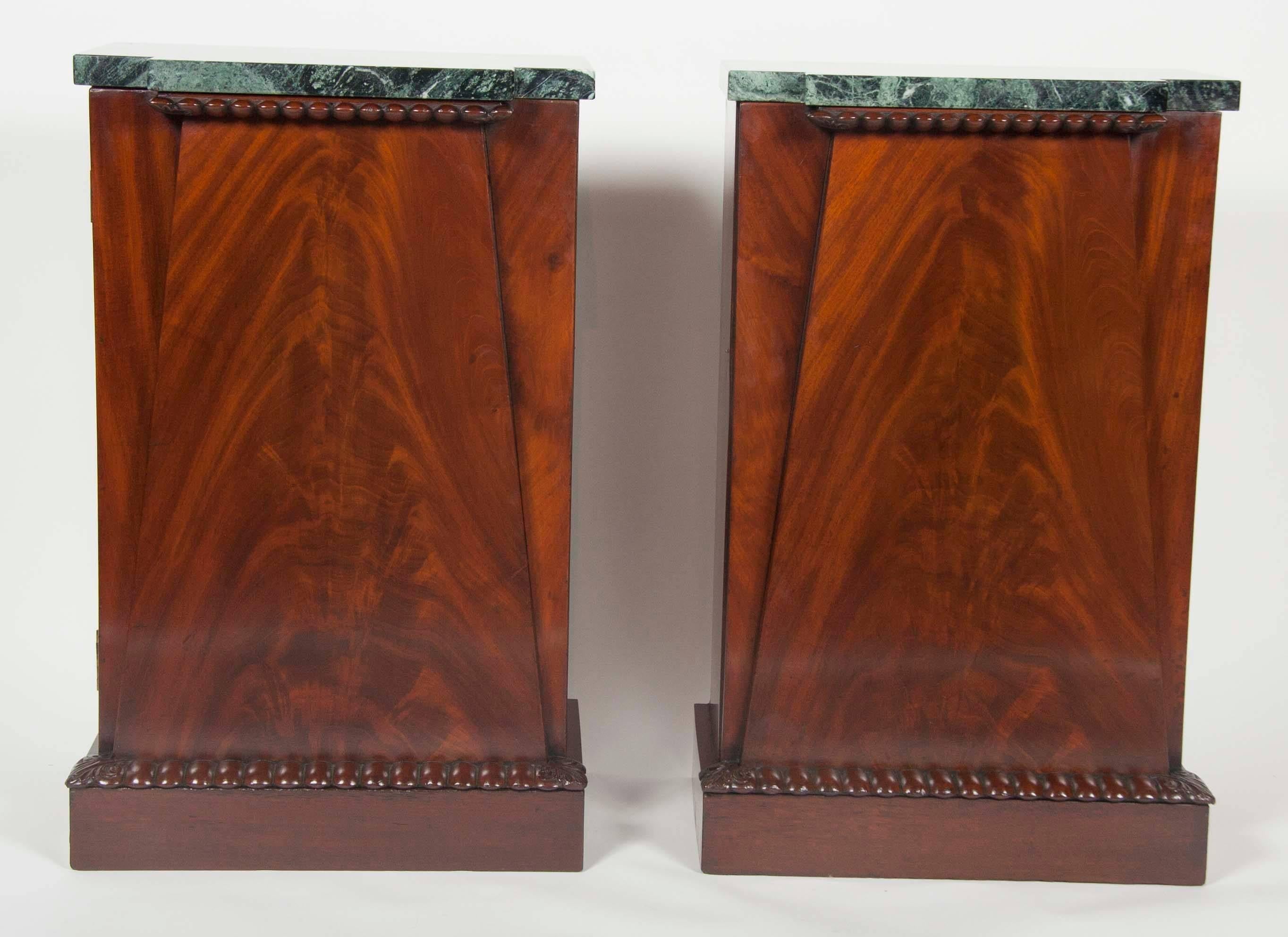 An unusual pair of American Empire mahogany veneer diminutive side cabinets with later marble tops. Doors open in opposing direction suitable for night tables.