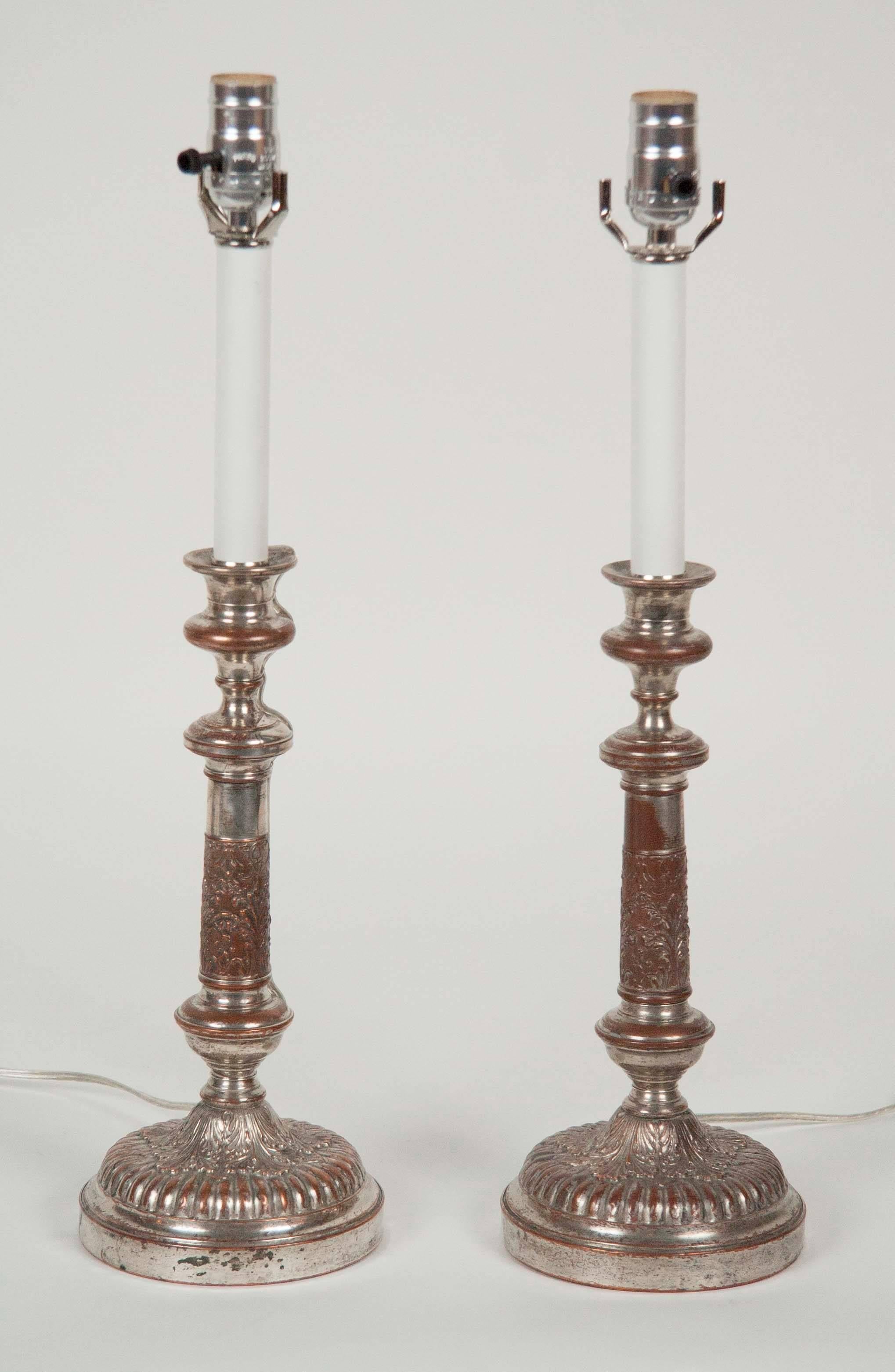A pair of silver on copper candlesticks having a decorated gadrooned base. Now electrified as lamps.