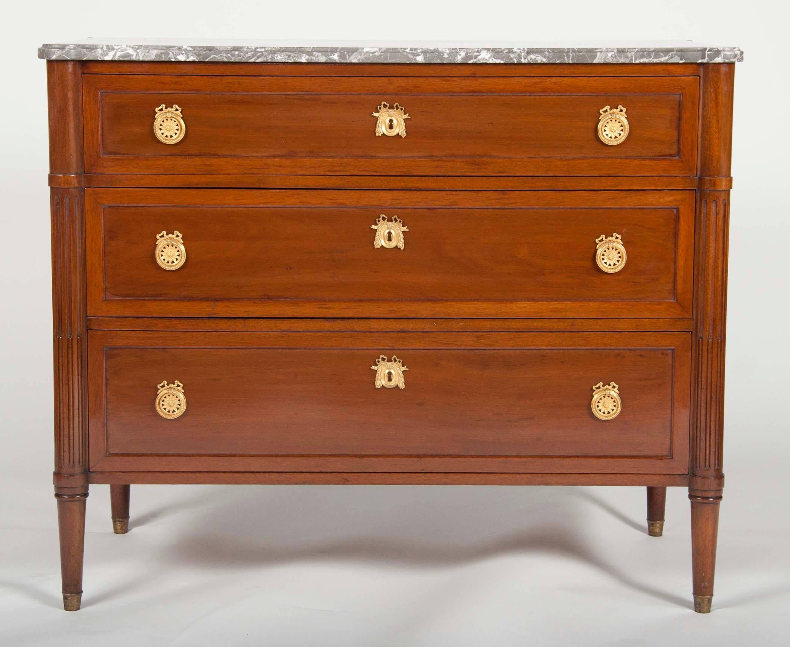 A pair of solid mahogany neoclassical style three-drawer marble-top commodes.