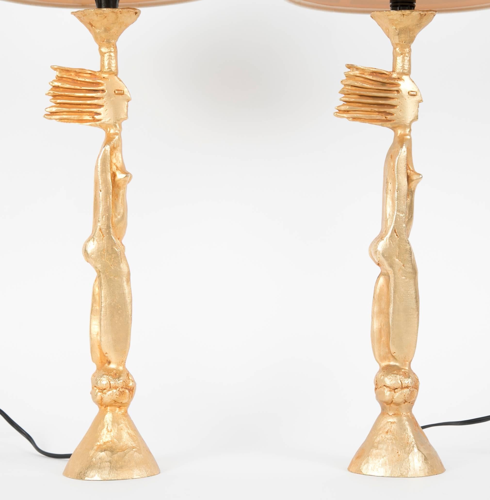 A matched pair of gold-plated metal lamps depicting nude women by Pierre Casenove. The lamps have their original shades, that do show some signs of age. One lamp retains more of its original gilding than the other thus the addition of the word