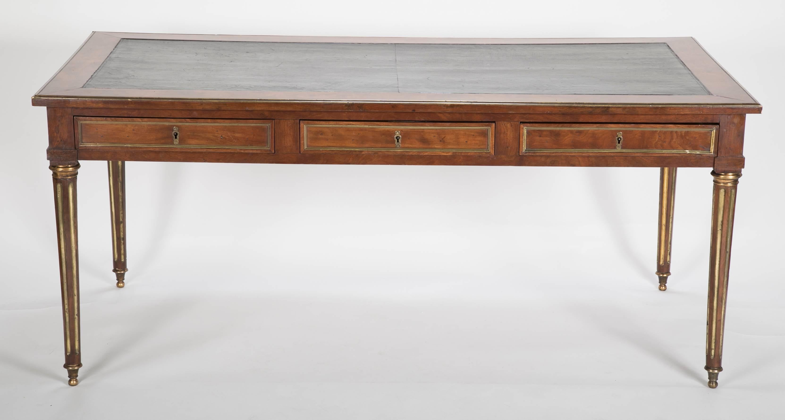 A large Louis XVI mahogany desk. This desk has gilt bronze mounts with bronze-mounted fluting running down the legs. It also has leather top and library slides on both sides.