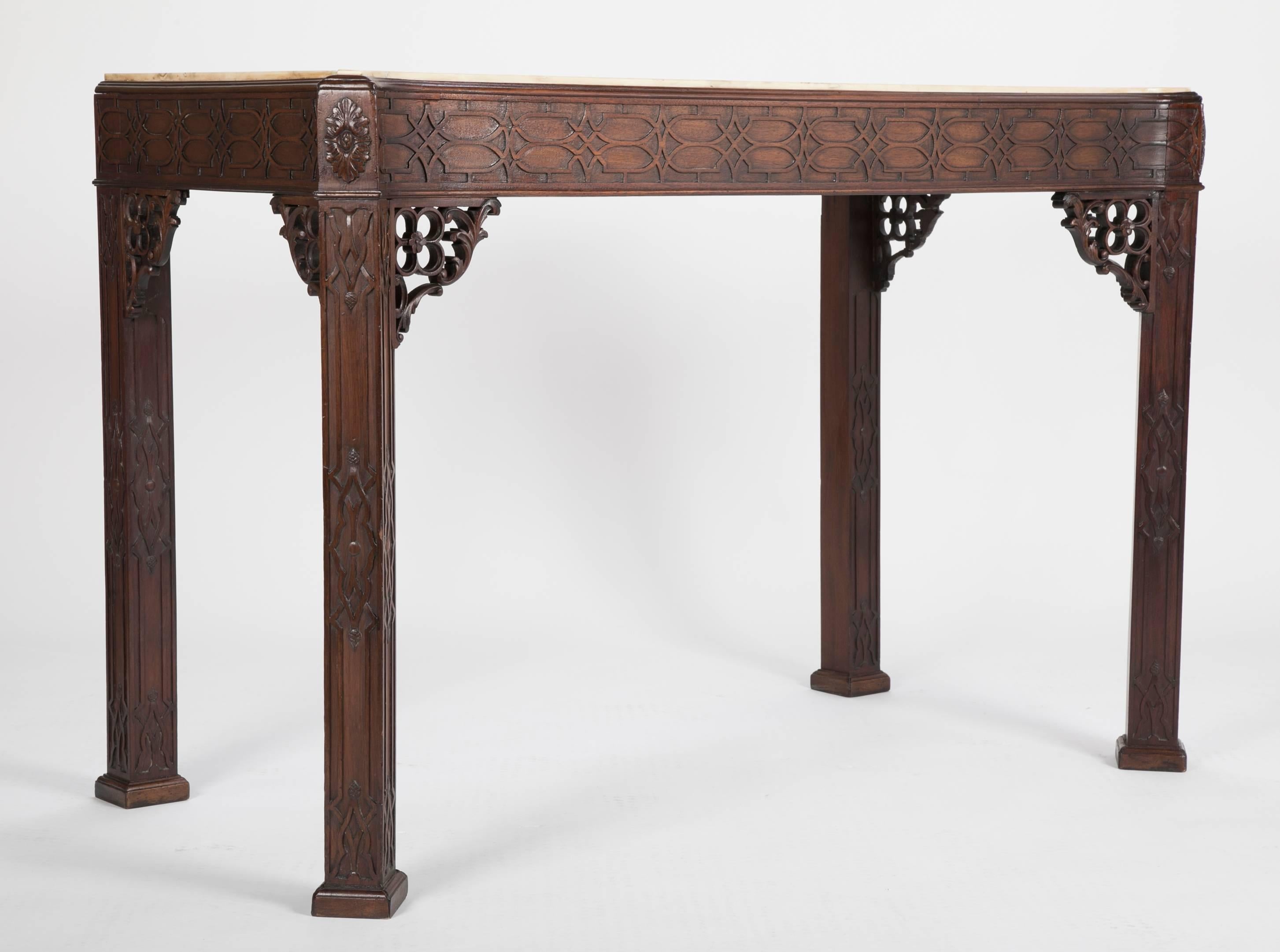 Late 19th century English console in the Chippendale style with marble top and black inlaid decoration. Heavily carved blind fretwork mahogany on bracketed columnar legs; the front legs presenting a broader apron give this console table an elegant