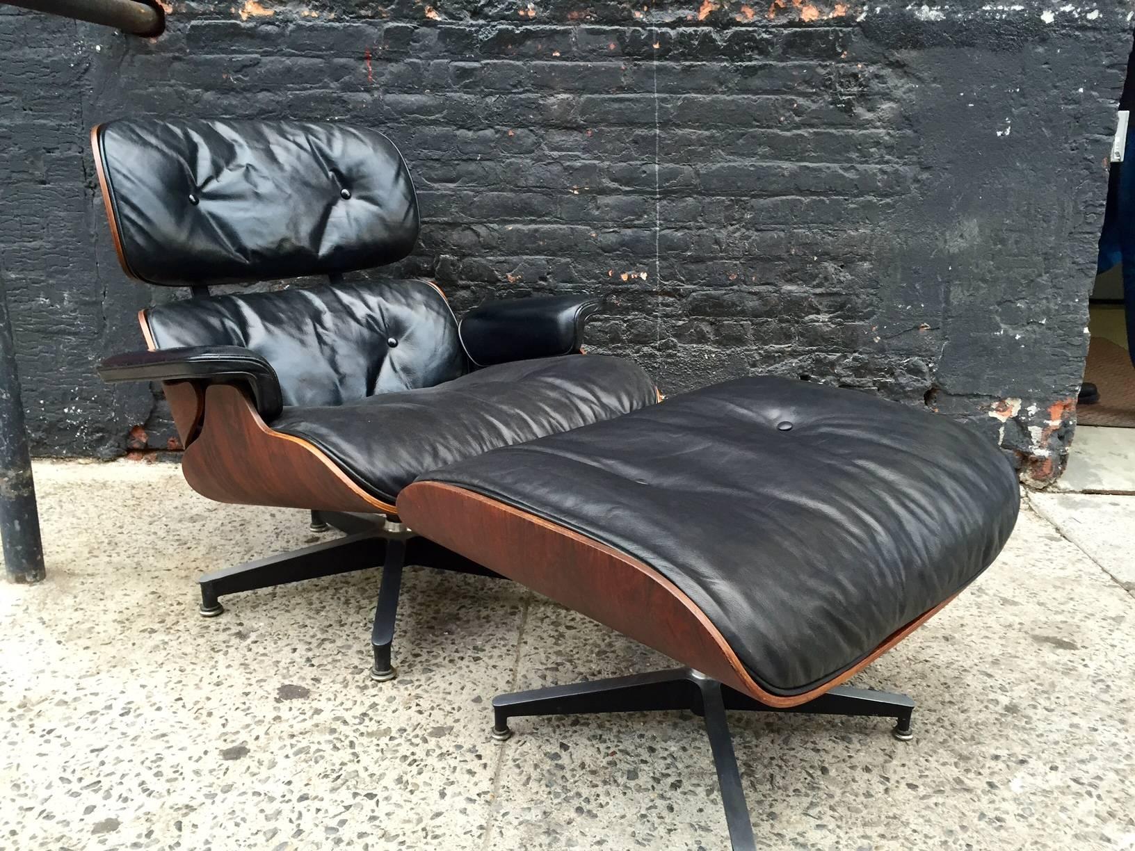 Charles & Ray Eames lounge chair and ottoman of rosewood with black leather upholstery. This is a second year edition, a coveted chair for Eames collectors, as evidenced by the three screws in the mounting plate under the arm.  

Dimensions of