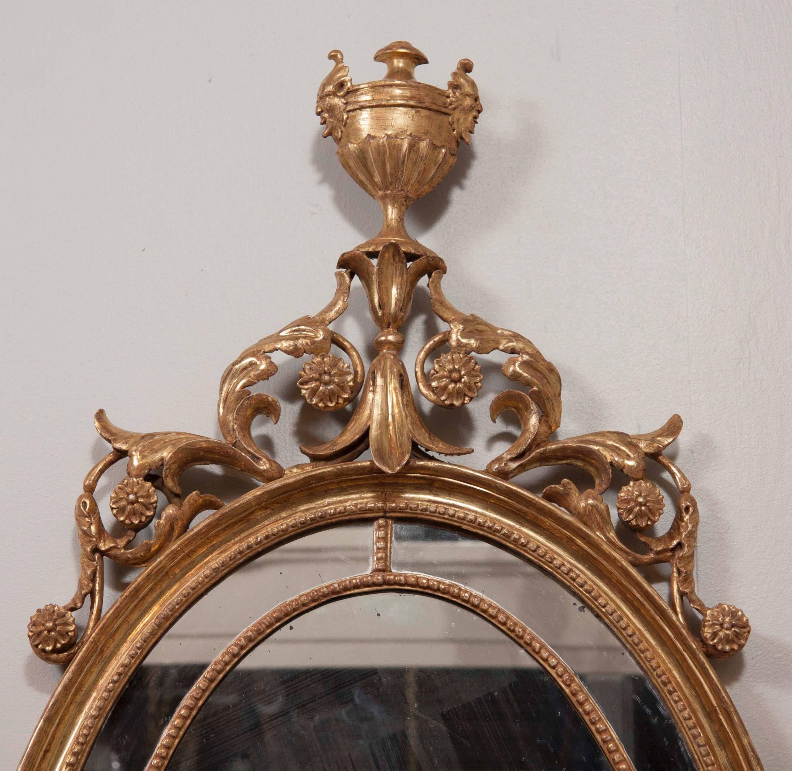 An English, George III, giltwood oval mirror surmounted by carved foliate scrolls and a carved giltwood urn.