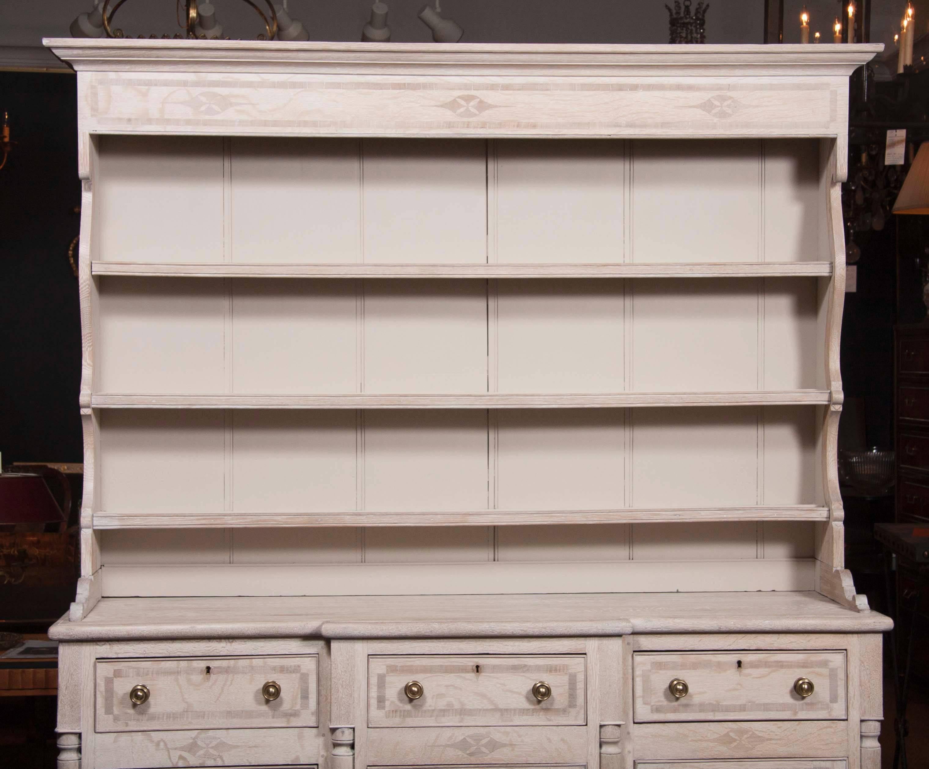 A large inlaid two part limed oak Welsh dresser with three drawers on top and three bottom doors including a central door composed of with fused drawers.