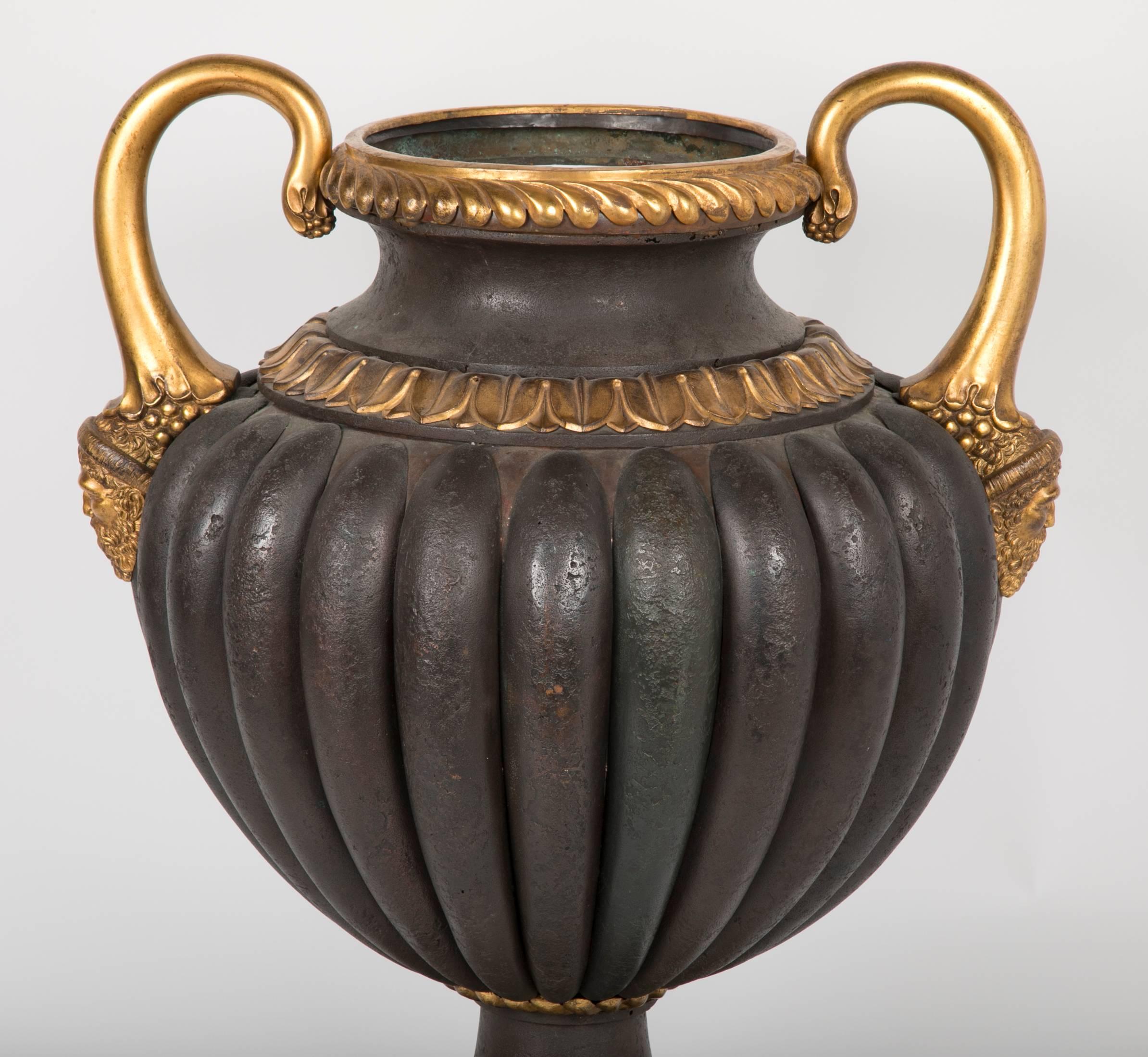 An Italian urn with gilt bronze handles have bearded men at there bases.  The urn has applied convex tole ribbing terminating at a pedestal base adorned in floral petals. 
24 ¼ in. (61.5 cm.) high; 19 in. (48 cm.) wide