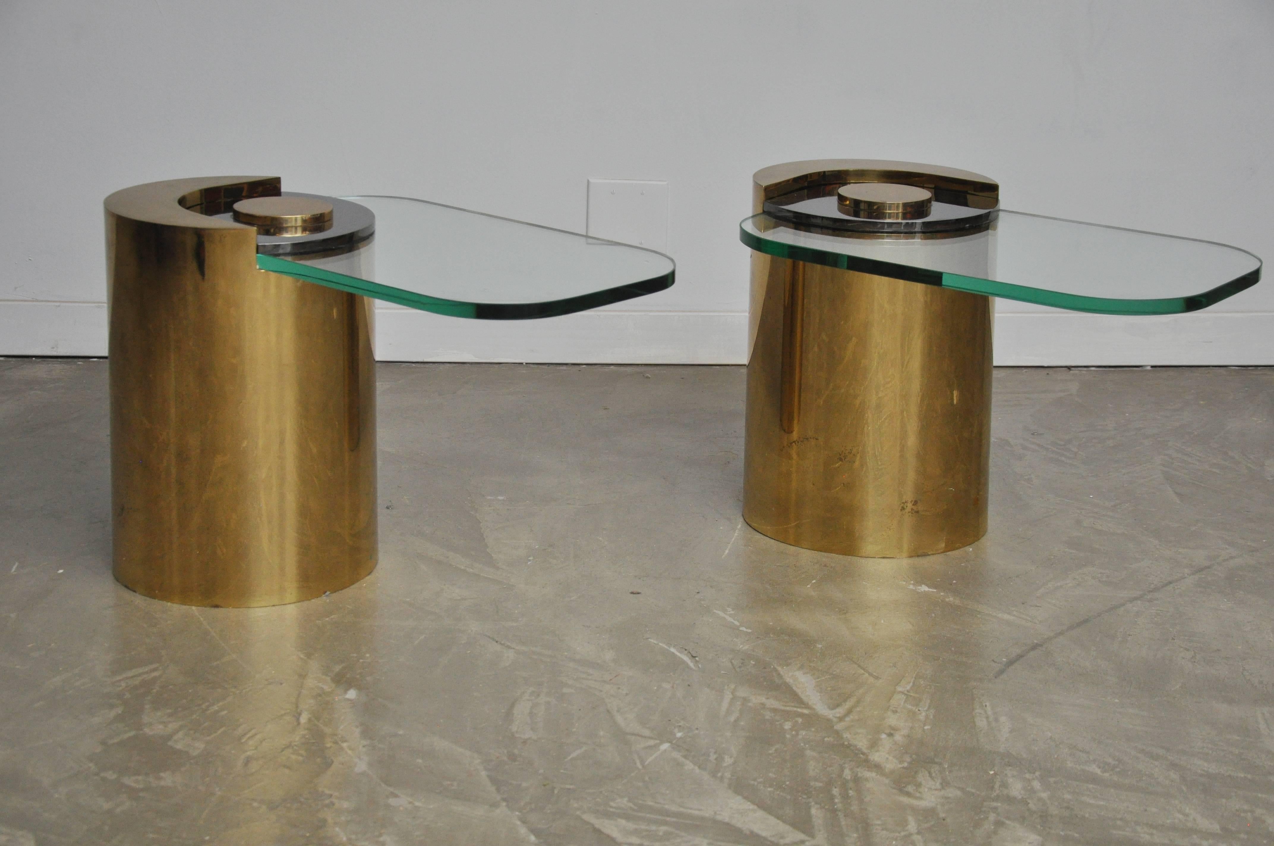 Pair of sculpture leg tables by Karl Springer. Brass bases with gun metal finish accent pieces holding cantilever glass in place. New glass, free of scratches. 
