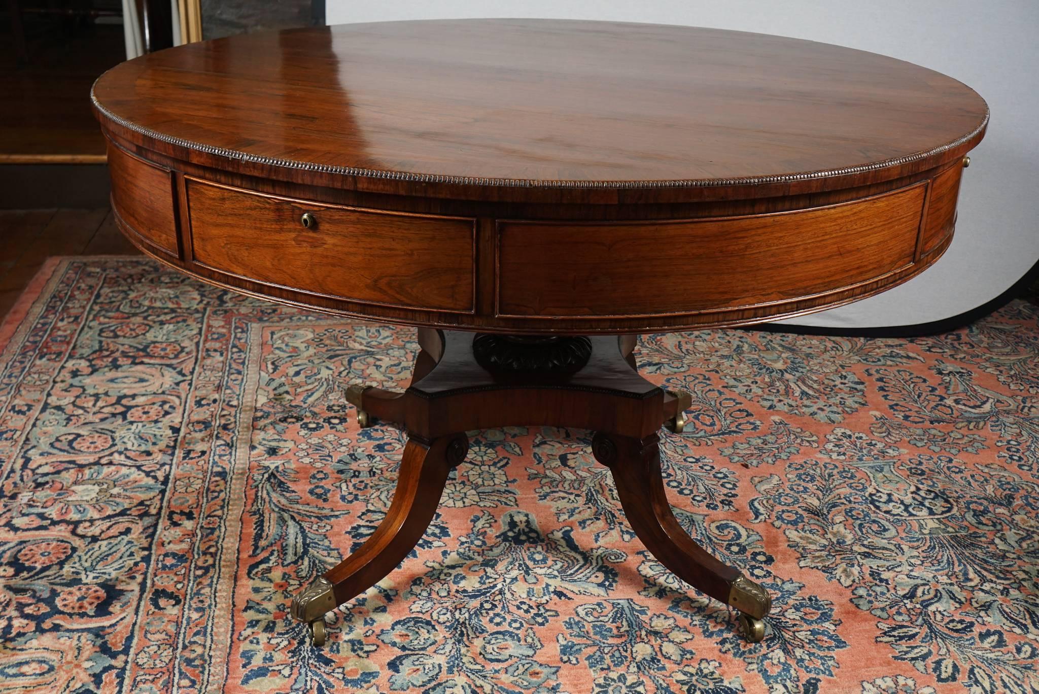 Nice English 19th century rosewood drum or center table. Rosewood top crossbanded with rosewood with carved edge over four working and four dummy drawers. Raised on a turned and carved pedestal with quadripartite base on four carved down swept legs