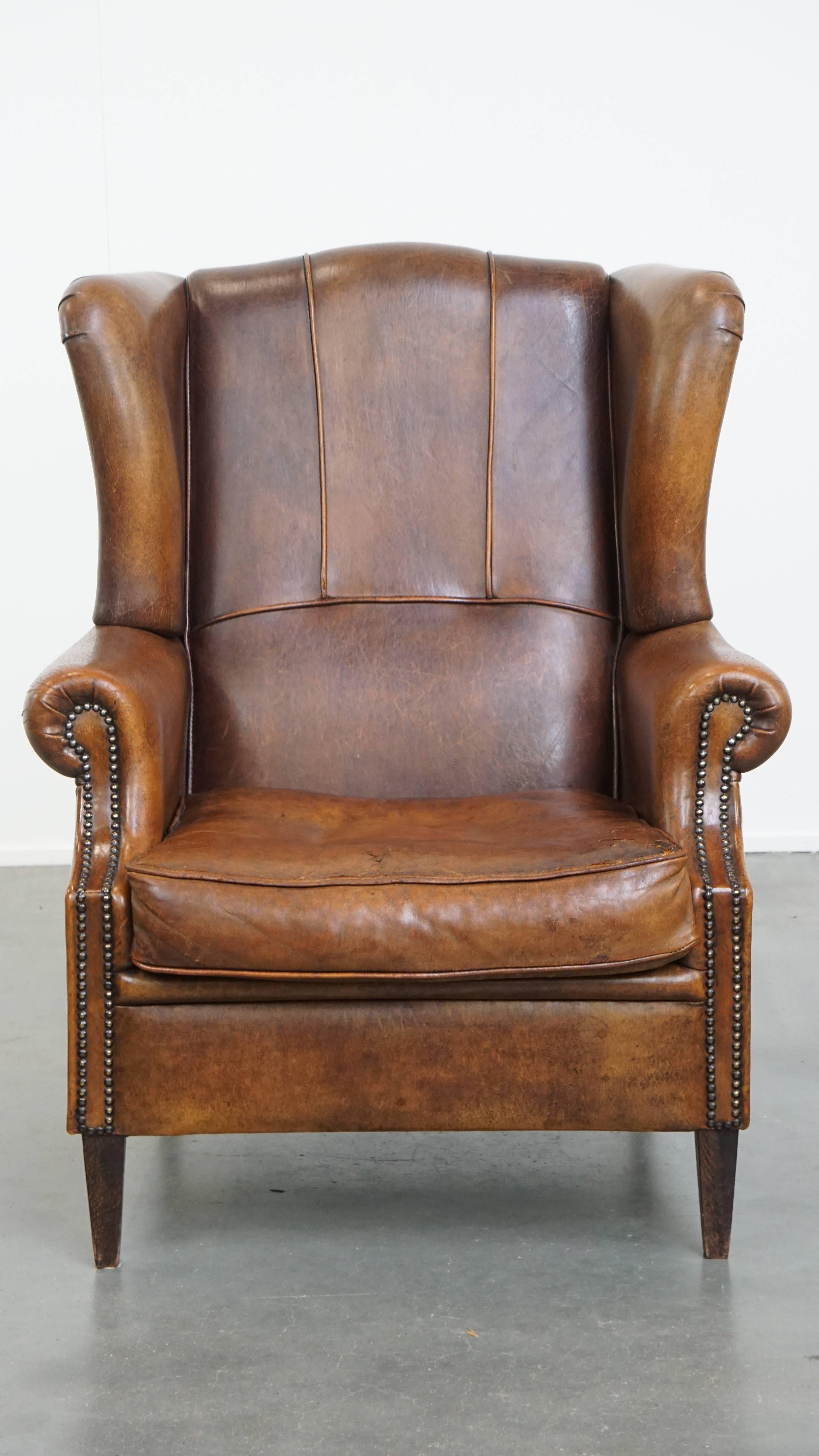Ce grand fauteuil à oreilles en peau de mouton peut être facilement placé dans presque tous les intérieurs. Il est bien fini avec des clous décoratifs et présente une belle patine. Ce fauteuil à oreilles est doté d'un coussin d'assise souple et