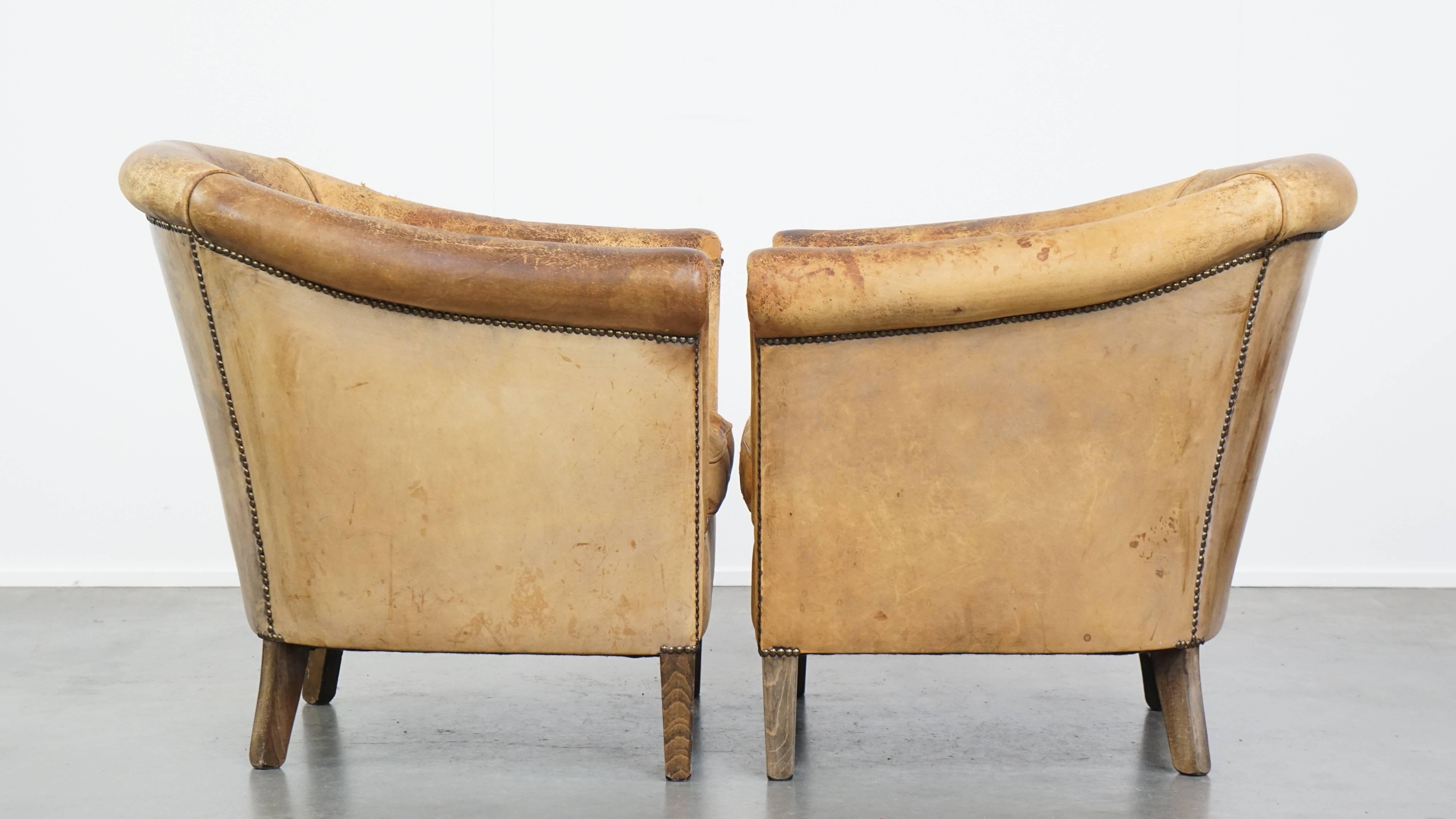 By Vintage propose un ensemble de deux fauteuils club en cuir de mouton vintage, bien usés, à l'aspect robuste et usé par les intempéries, créés par Nico van Oorschot. Ces fauteuils club en peau de mouton sont pleins de caractère. Ils présentent des