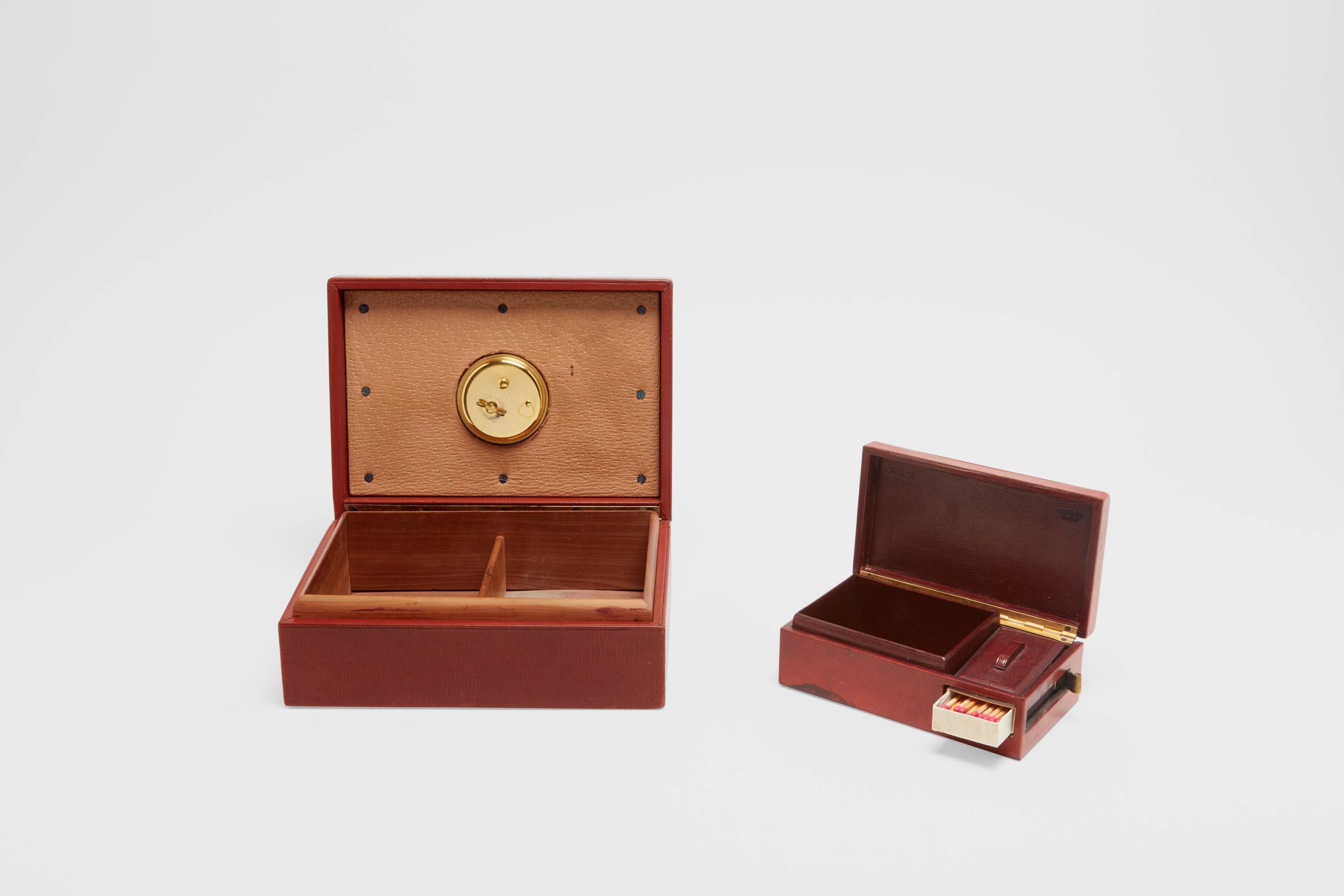 A wood leather covered cigar box with a fully working clock in the lid, along with an accompanying wood leather covered cigarette box with enclosed match box with striking area to the side. This is an exceptional and very rare set by two of the most