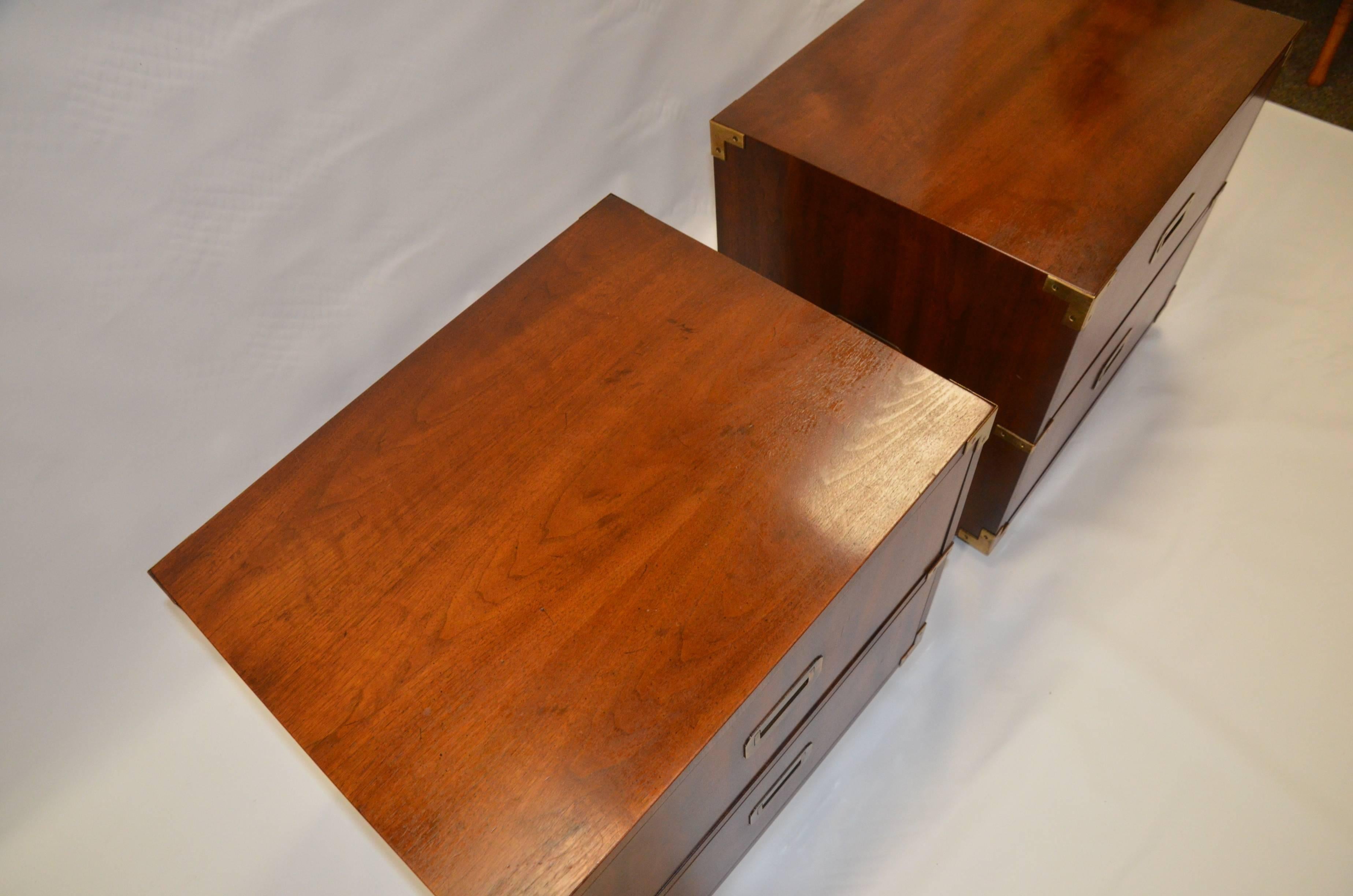 Pair of vintage Campaign style nightstands by Henredon. This pair is crafted out of walnut and feature recessed brass pulls and brass corner hardware. Each nightstand has two deep dove-tailed drawers for storage. They sit upon block feet and feature