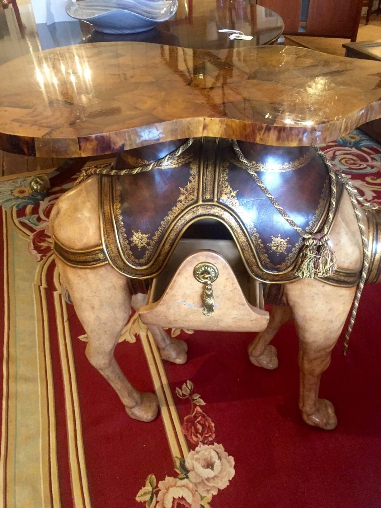 Dramatic over the top serving table having a camel figure as the base with amoeba shaped table top surface, polychrome paint decorated and one accessory drawer with fancy brass tassel hardware.