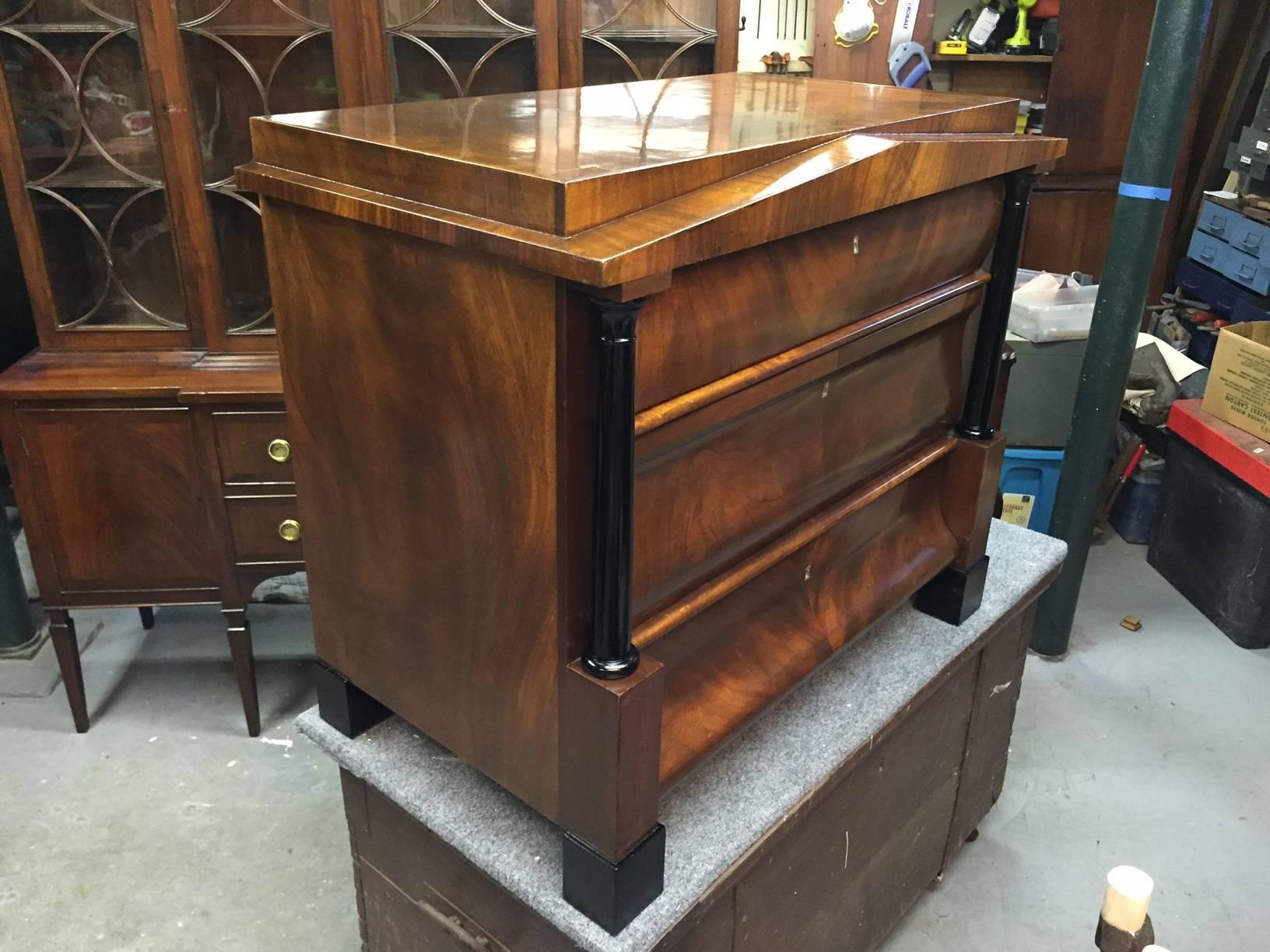 Rich lustrous pair of cabinetmaker made mahogany and ebonized commodes in the Biedermeier style with three drawers and neoclassical columns and triangular decorative front. Lovingly French polished.