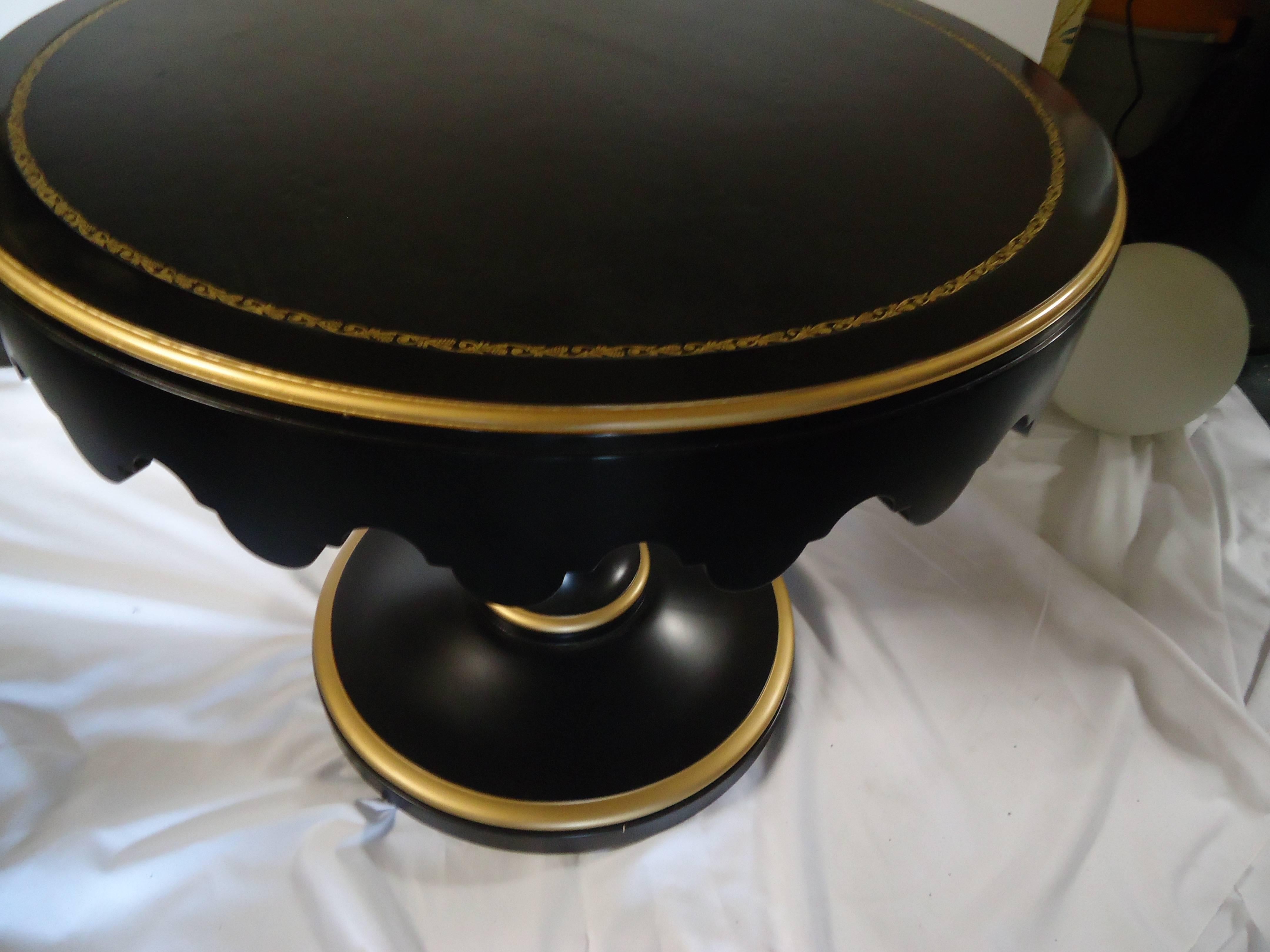 Dramatic round side table or small round table having ebonized wood with gold leaf detailing and black and gold tooled leather top. About 8 years old.