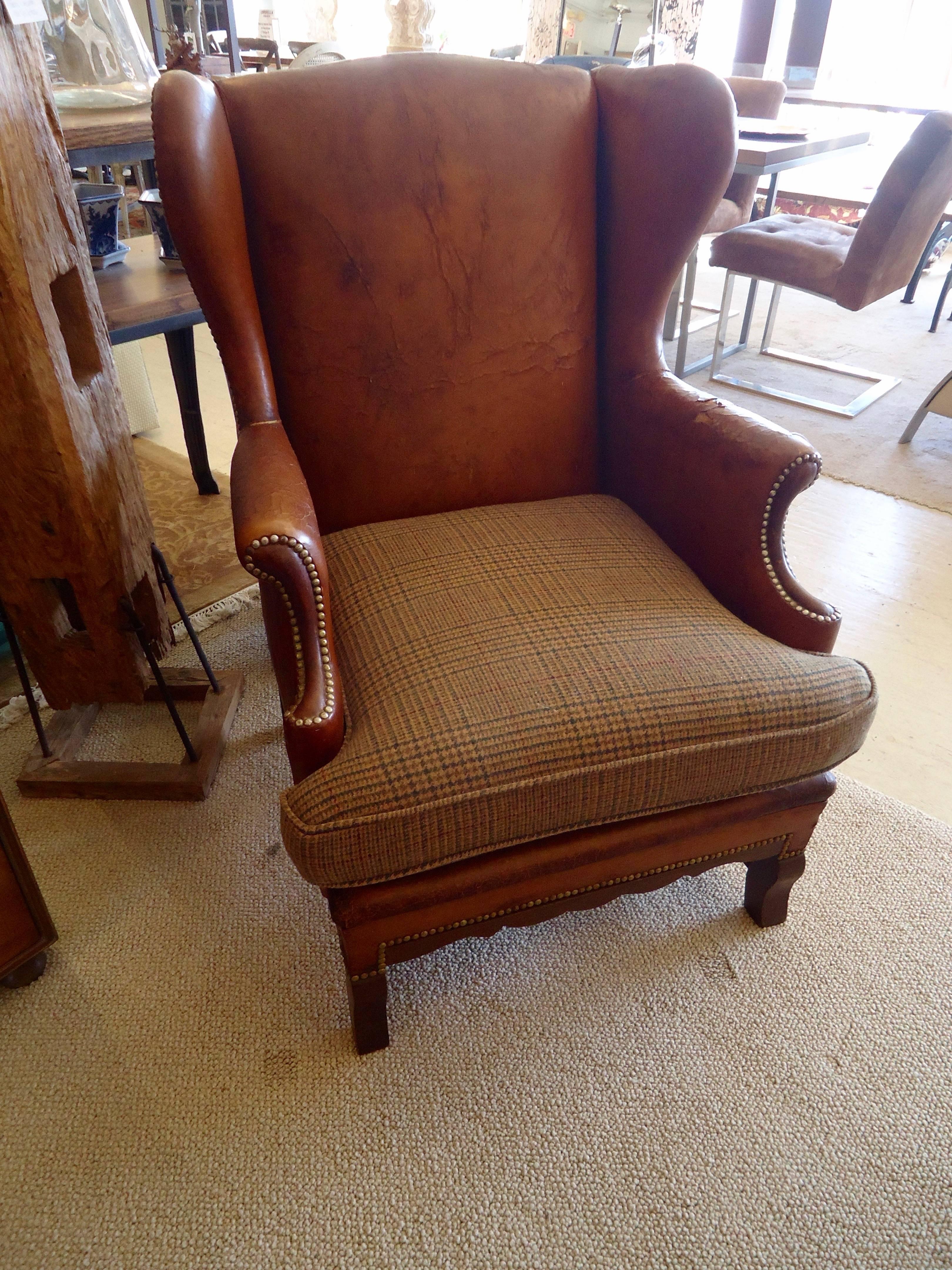 Distressed early 19th century leather wing chair with mahogany base, brass nailheads and a newly upholstered Ralph Lauren wool plaid seat cushion.
Oozing with character. Measures: Seat depth 23