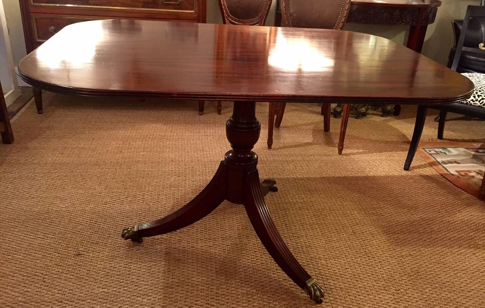 English Regency mahogany tilt-top breakfast table, circa 1840, the rectangular top with rounded corners and a reeded edge, resting on a turned baluster and a tripod base with reeded saber legs ending in brass paw feet with casters.