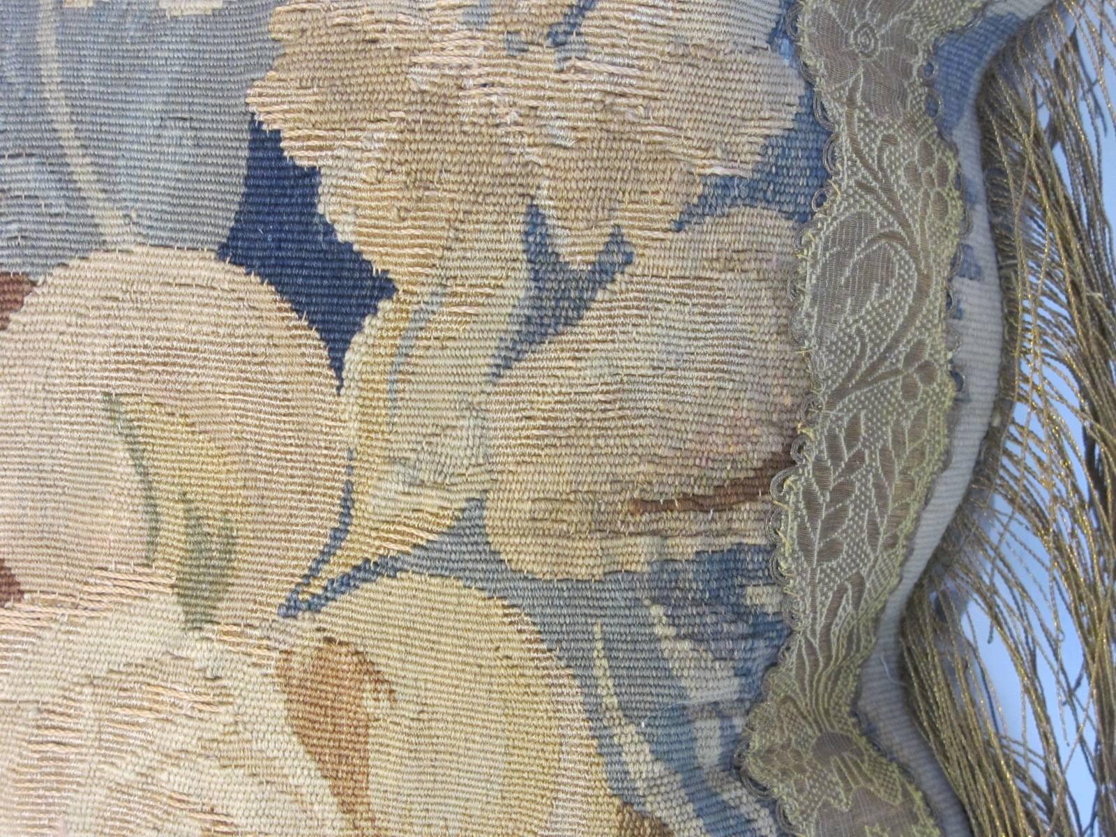 A pillow crafted from a circa 1880s Aubusson tapestry fragment depicting flowers and fruit, embellished with antique metallic trims, backed with coordinating silk velvet, muted shades of blue, browns, taupe.
 