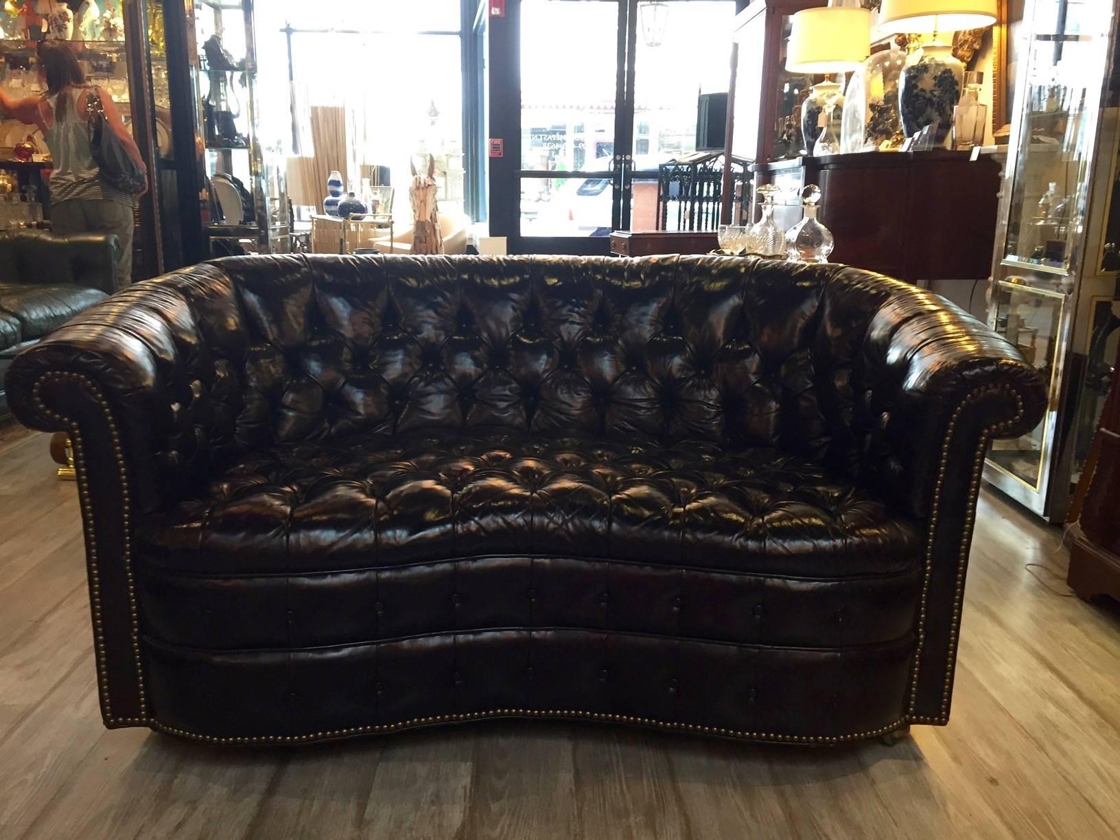 Very rare find in rich dark brown leather, this wonderful curved tufted Chesterfield loveseat oozes character. Brass hobnails define the sensual shape of the base and arms and it's easily moved on brass casters.