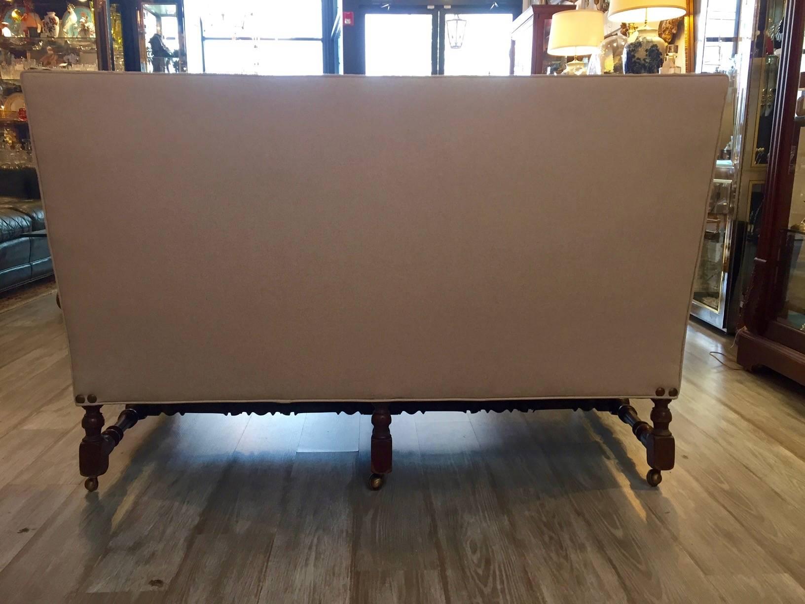 Great looking sophisticated vintage loveseat that sits on a gorgeous turned mahogany frame with brass casters, freshly upholstered in cream linen and stylishly finished with big brass hob nailheads around the bottom. One comfy seat cushion in soft