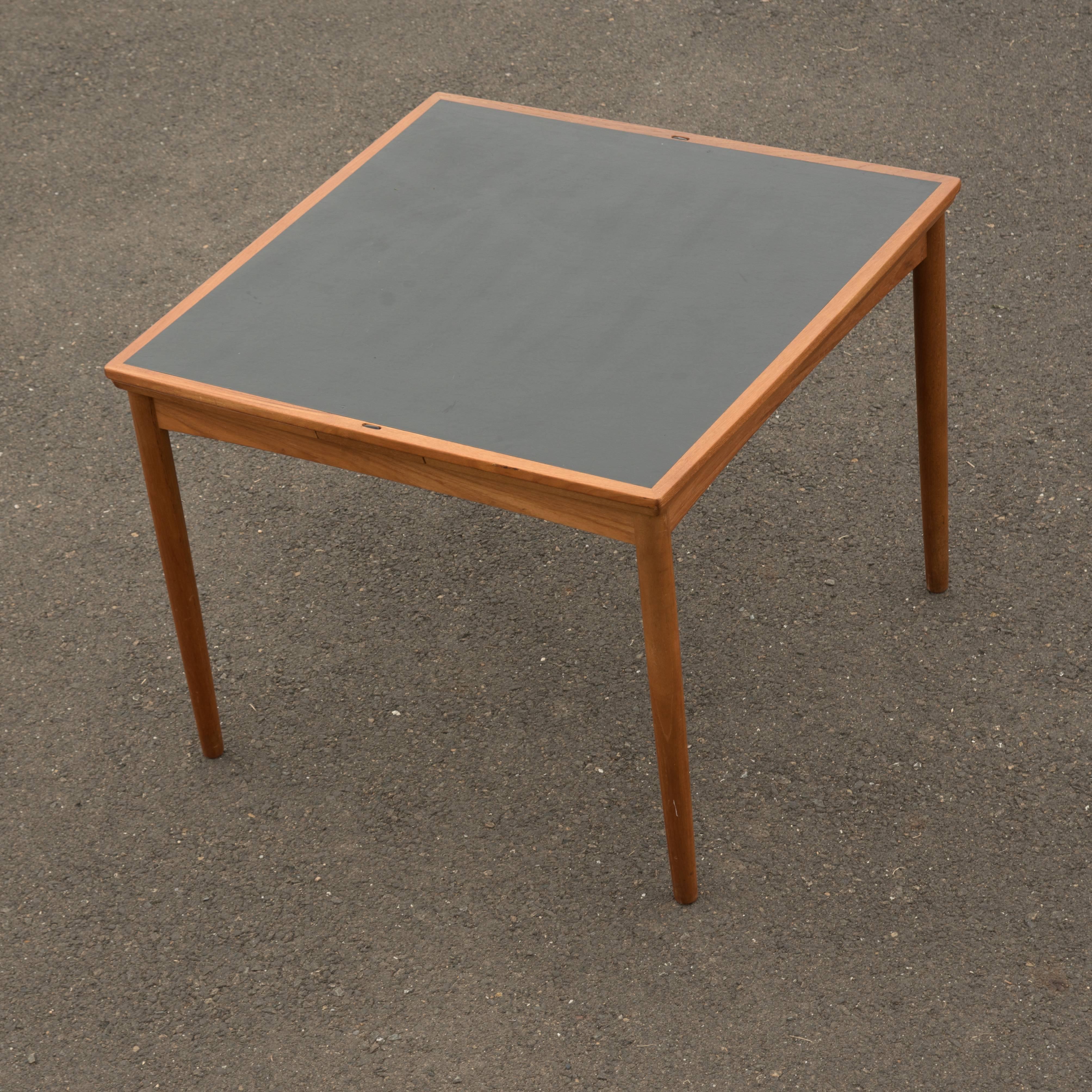 Sleek Mid-Century Modern Danish designed versatile table, made of light brown teak with a top that that flips over and becomes a black faux leather surface for playing cards or games. Two leaves easily slide out and up on two sides to create a