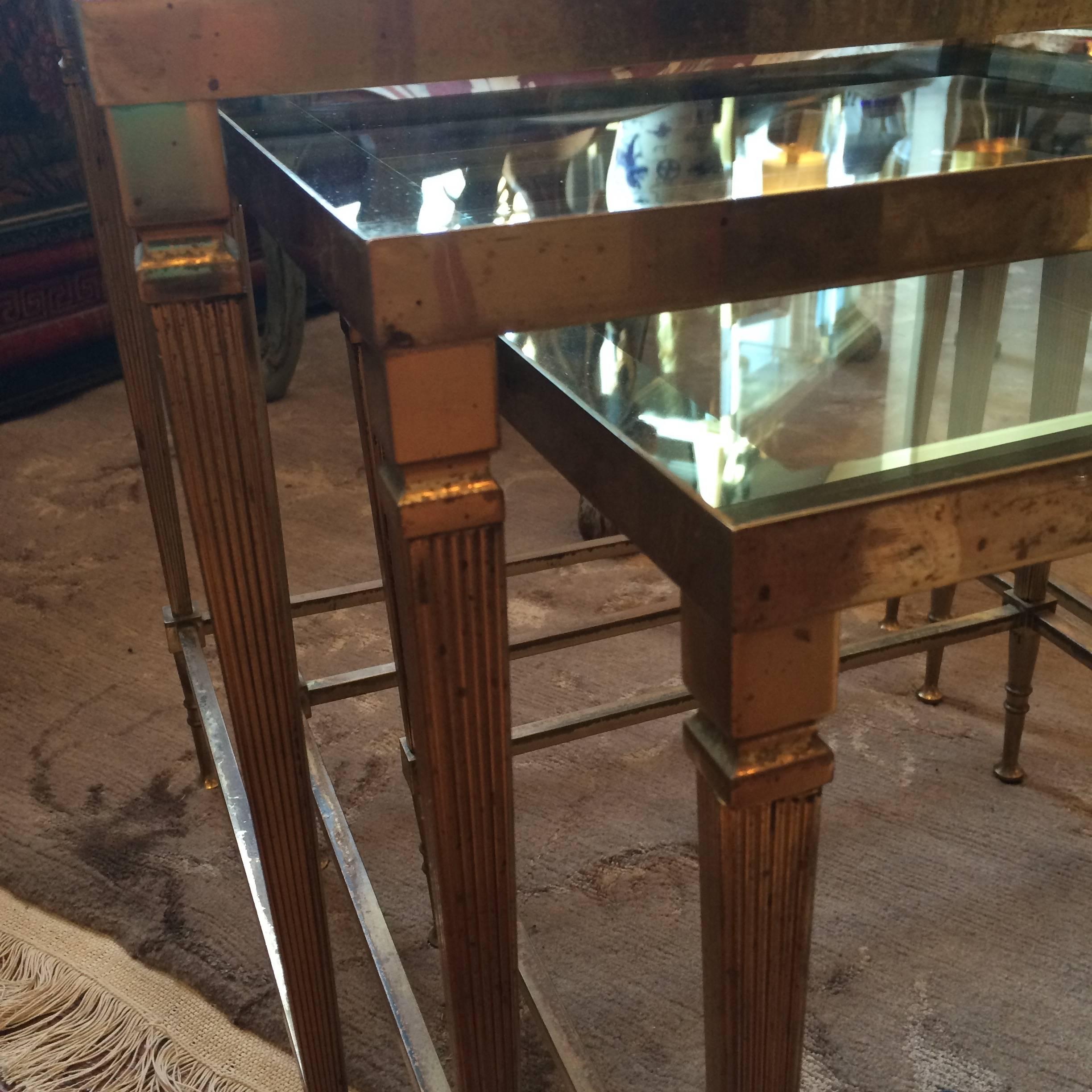 Three brass nesting tables with glass inset tops. Glass has silver mirrored edge detail. Fluted tapered legs with a neoclassical feel.