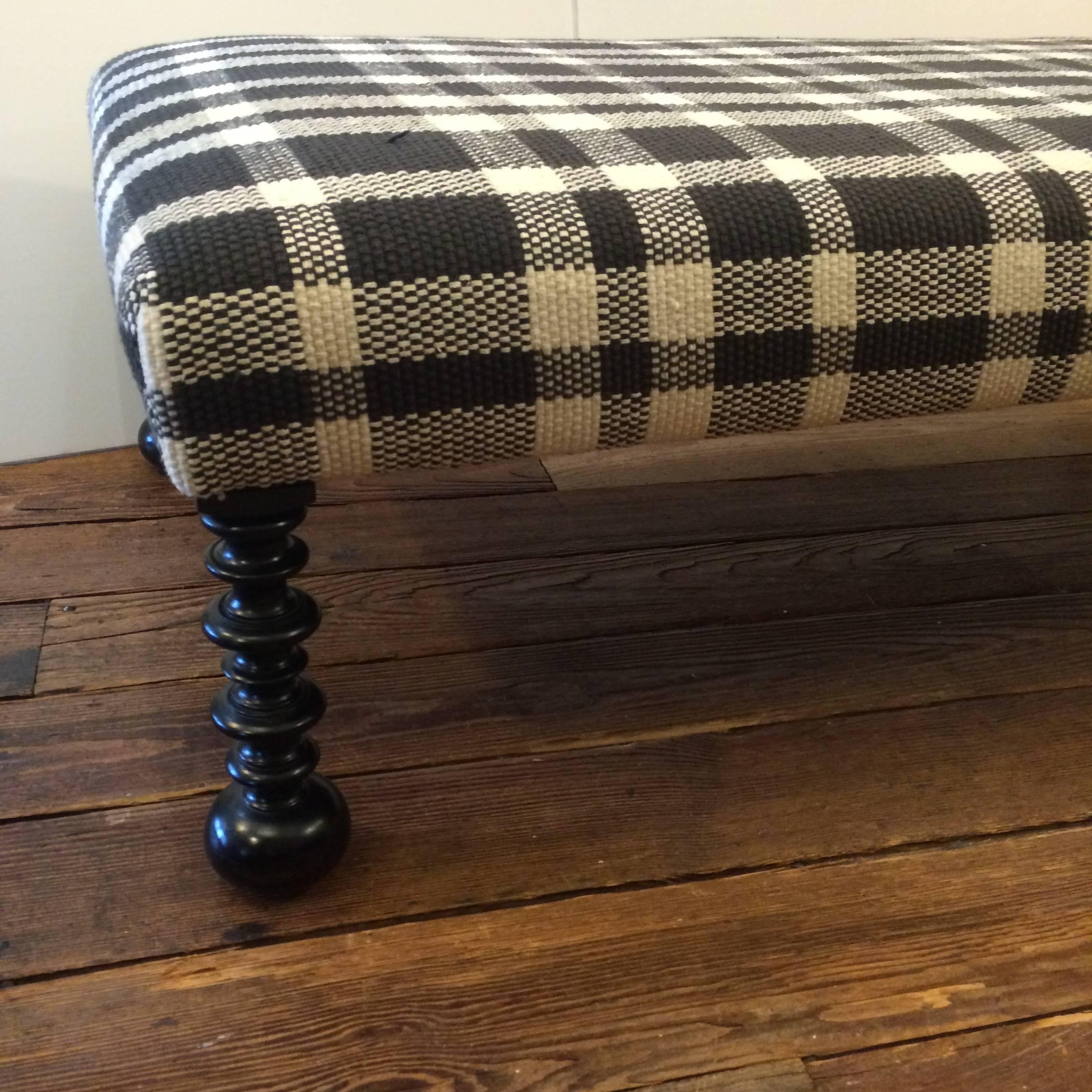 Handsome rectangular ottoman or coffee table with turned ebonized wood feet and upholstered in a striking Dhurrie black and white plaid. Perfect condition. About 10 years old.