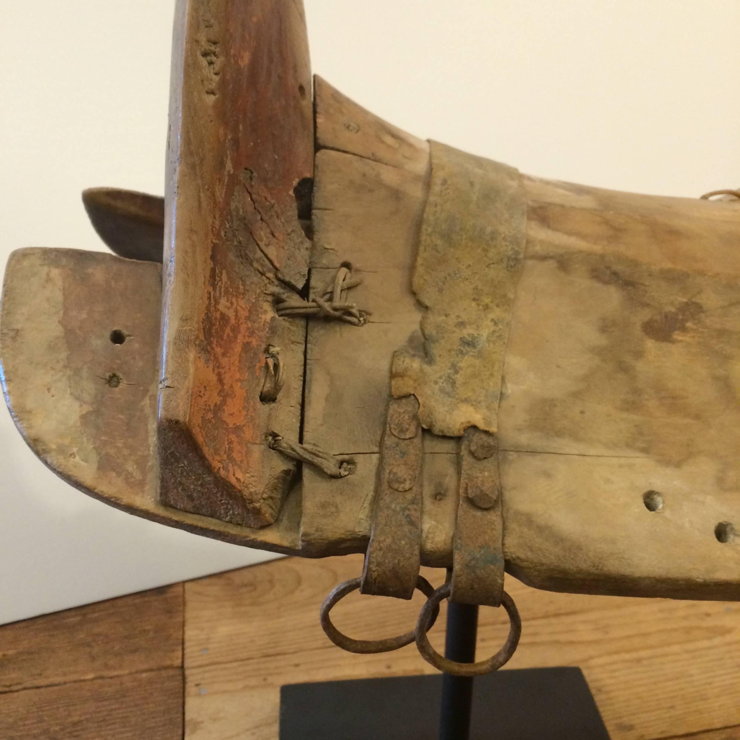 Wonderful found object sculpture oozing with character that's an old wooden Chinese pony saddle with distressed surface, leather straps and rawhide adornments, mounted on a contemporary black metal stand. We don't know for sure how old it is, but it