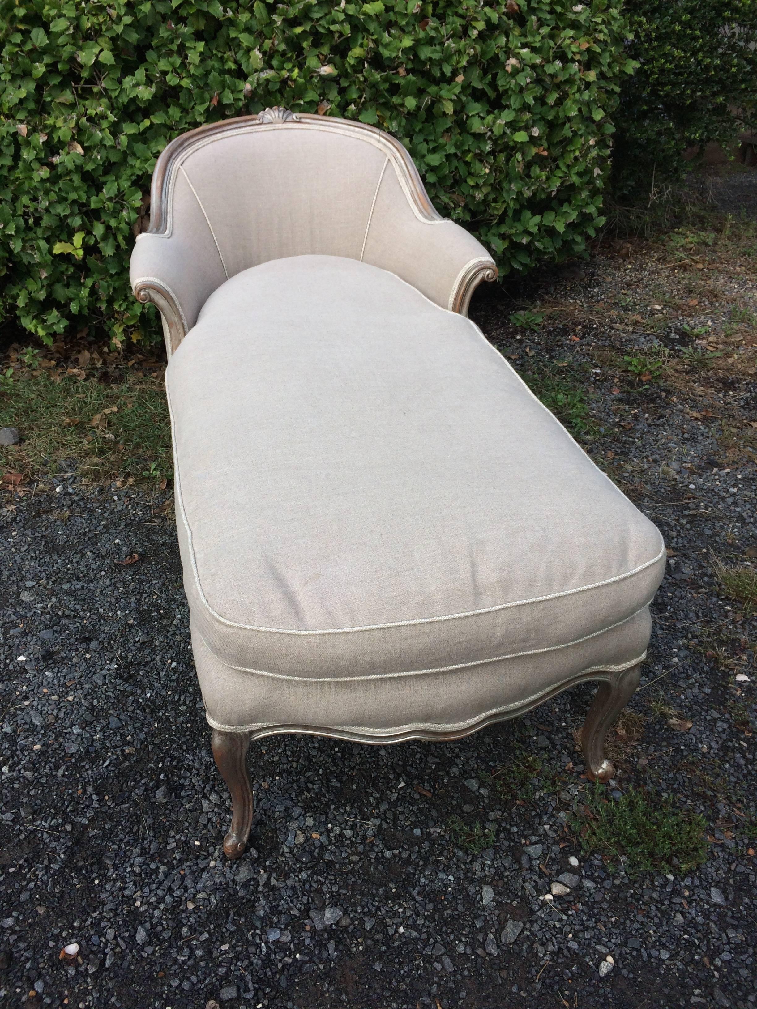 Lovely French 1940s chaise having silver giltwood and carved frame with shell embellishment at the top, upholstered in neutral Belgian linen with a comfy down cushion. Measures: Seat is 53