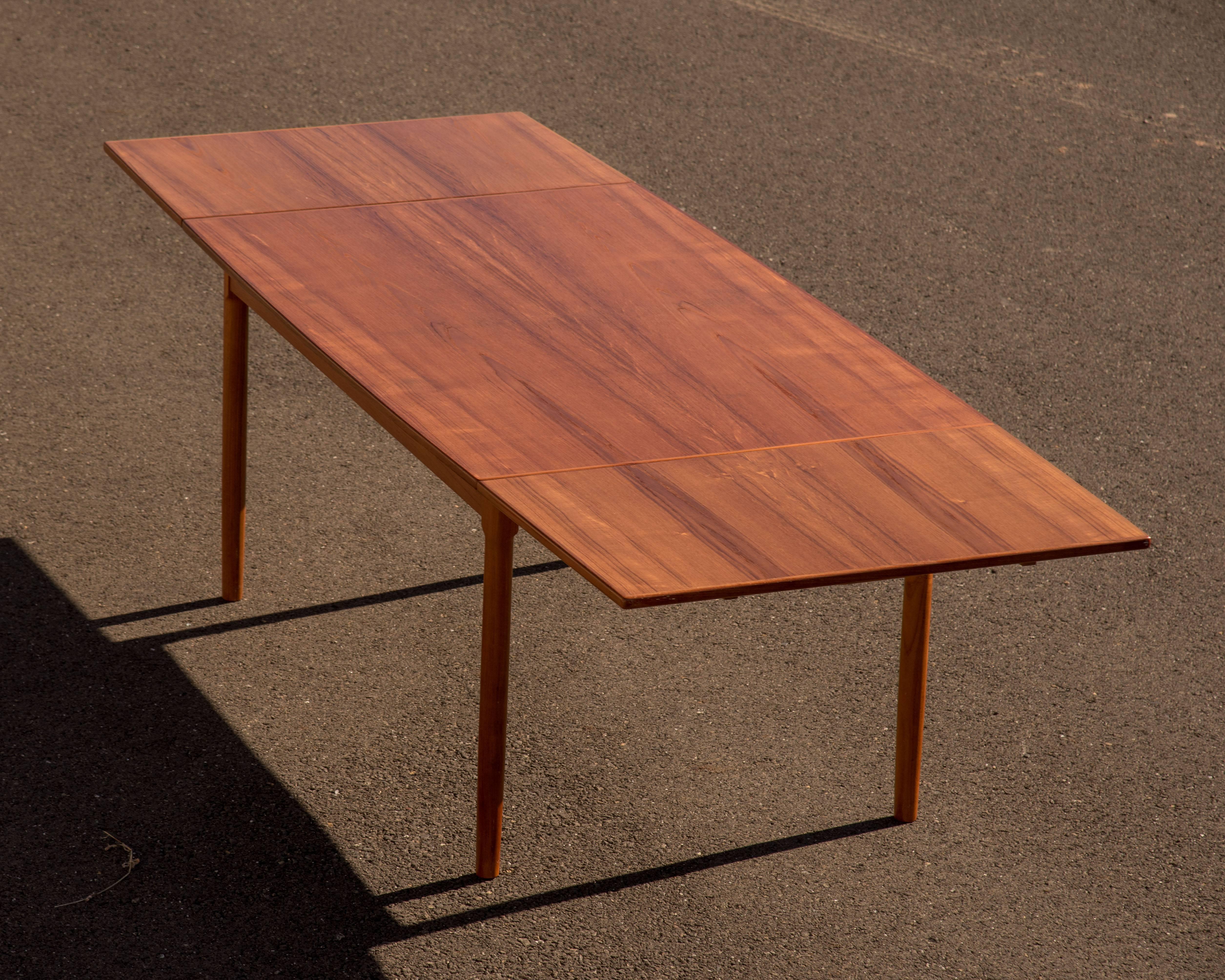 Stunning Danish designed teak dining table with two sleek slide out leaves on each side to allow for comfortable seating for up to 10. In it's closed position the table comfortably accommodates six. There's an elegant slight taper to the surface