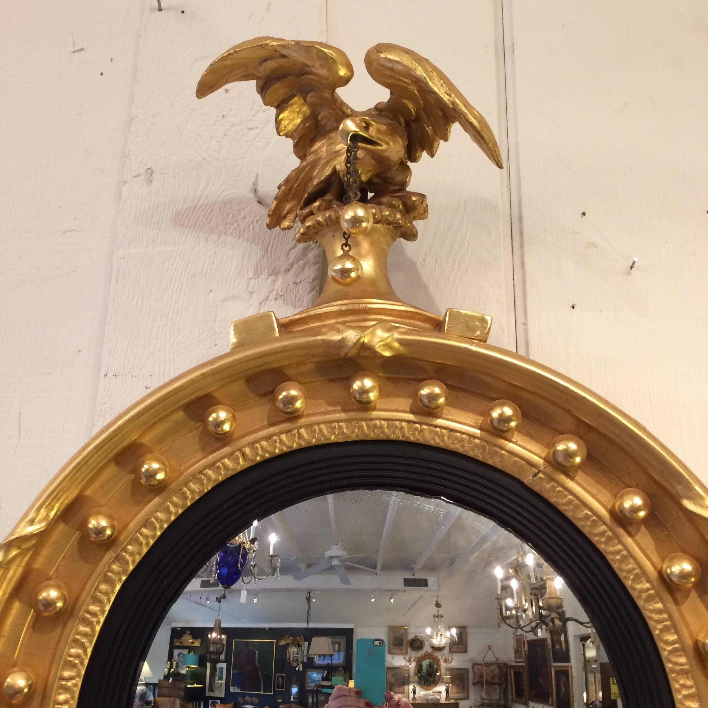 Gorgeous example of a giltwood fully restored Federal mirror with circular cove carved frame with inset gilded spherules, proud eagle at the top that dangles two glistening balls from it's beak, with an adornment of leaves at the bottom.