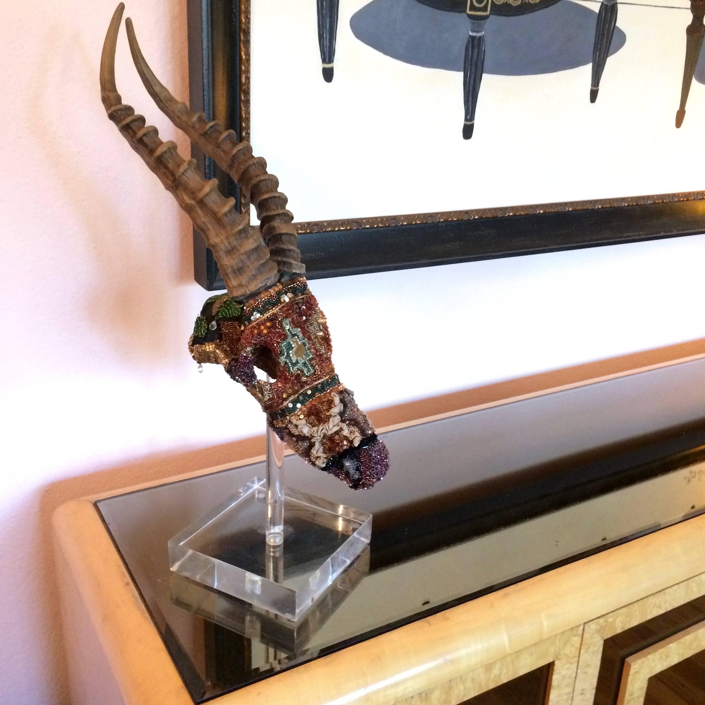 Richly bead encrusted faux skull sculpture adorned with vintage bits and pieces of jewel like fabric, mounted on a Lucite stand.
By mixed media artist Fay Sciarra.