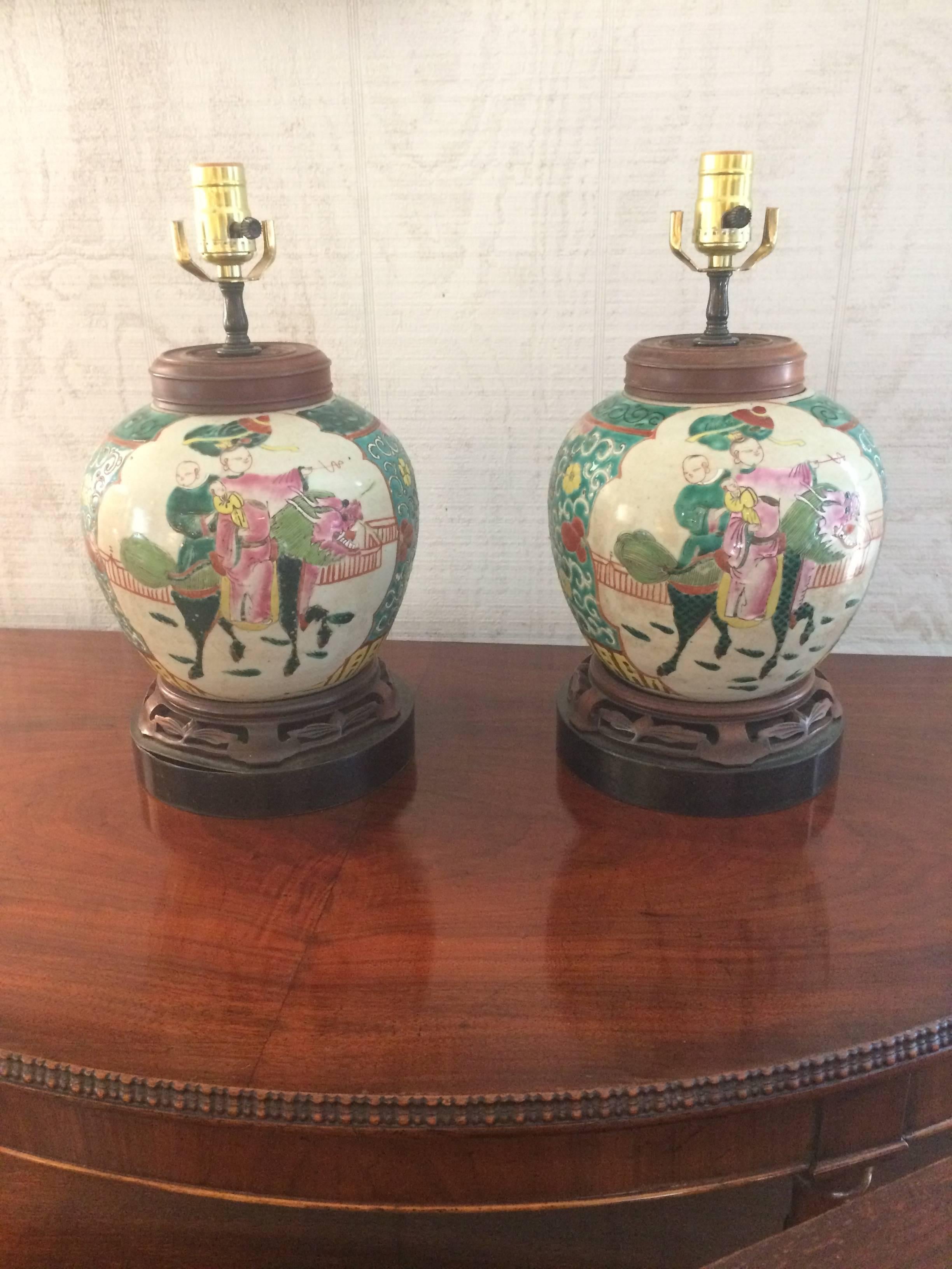 Elegant pair of Chinese rose medallion table lamps having beautifully embellished ginger jars with royal couple on horseback, carved rosewood caps and rosewood and bronze bases.