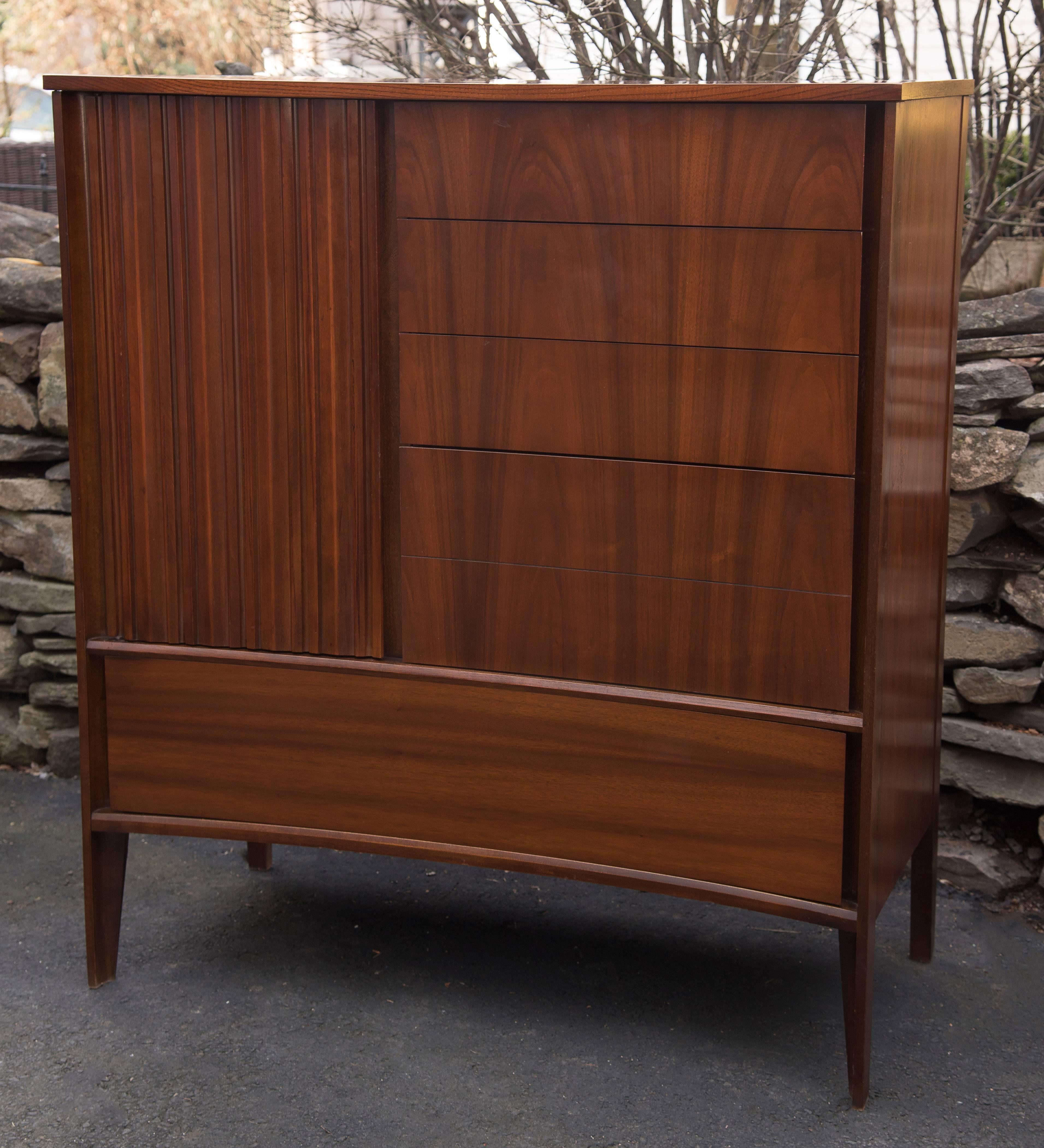 Mid-Century Modern Danish walnut high chest of drawers or dresser by Edmond Spence for Strata having a sleek subtle concave bow shaped silhouette, four stacked drawers on the right that are opened from the sides, a cool accordian shaped door on the