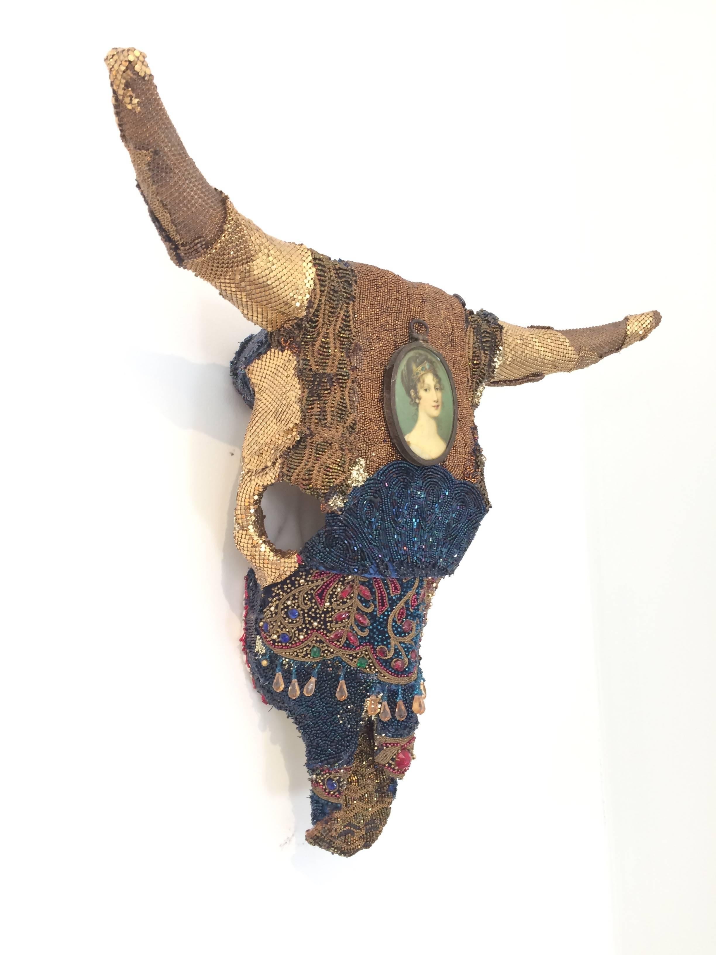Magnificent gem of a wall sculpture in the shape of a skull, incrusted with layers of beading from vintage remnants, gold lame antique purses, a lovely painted miniature, and other treasures.
