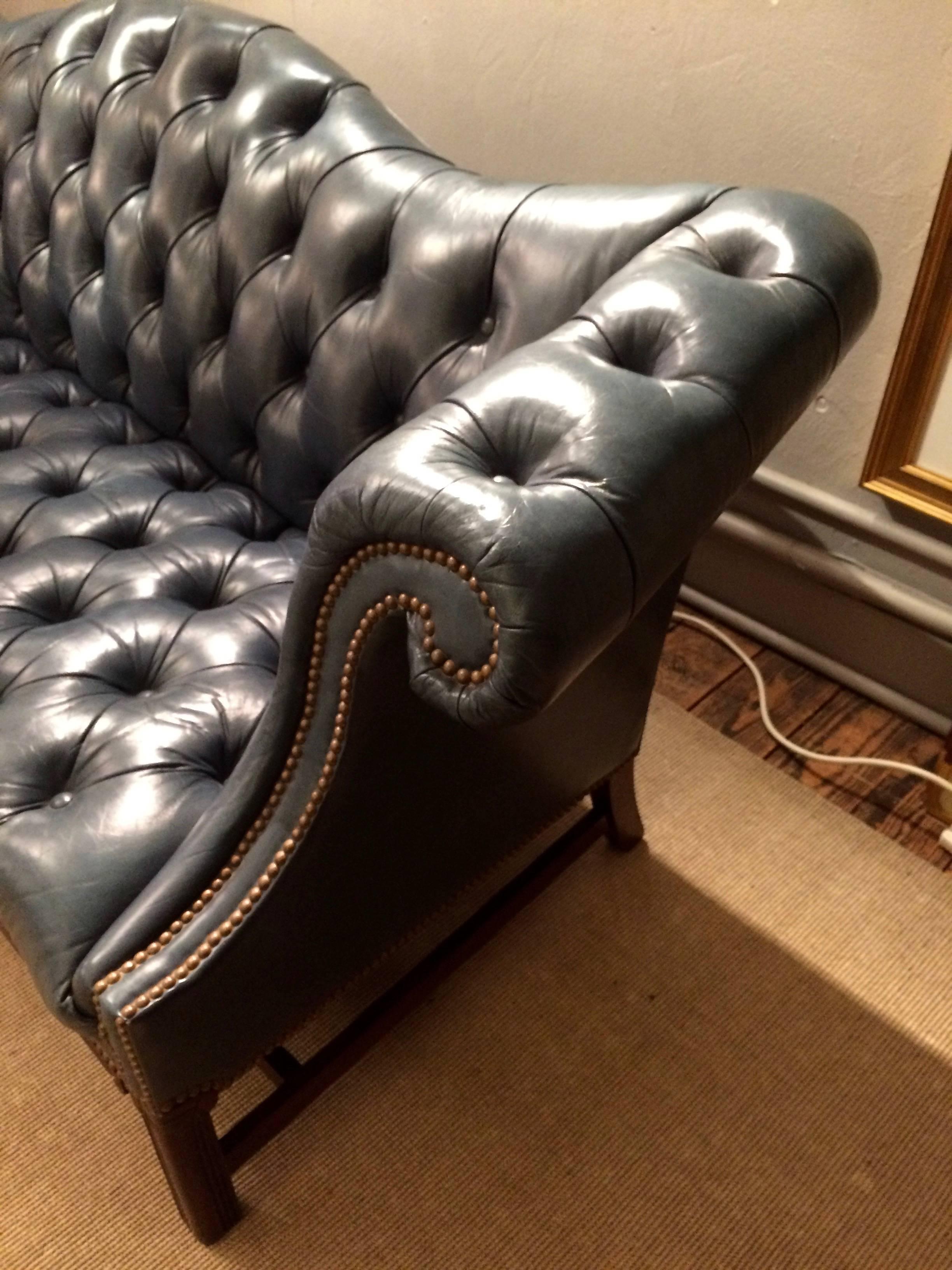 Great looking Chesterfield sofa with curlicue arms and carved mahogany Chippendale style base. Leather is a soft tufted grey blue with natural vintage patina, finished with brass nailheads.
