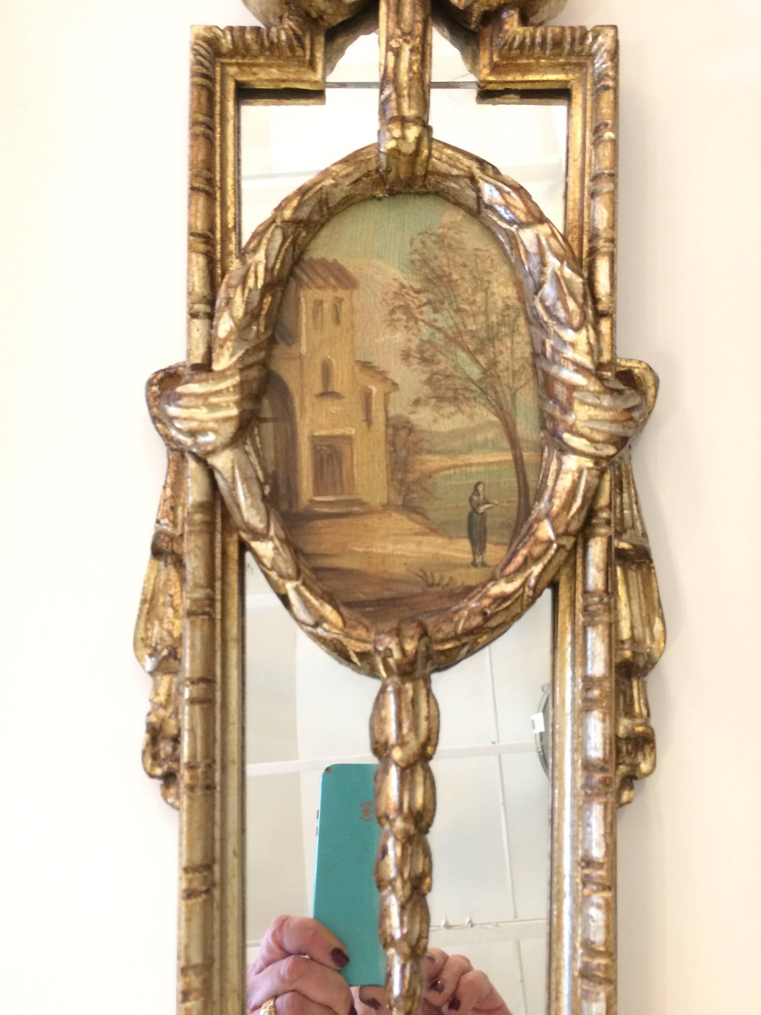 Elegant pair of elongated decorative mirrored panels having carved silver gilt frames and hand-painted inset landscapes.
