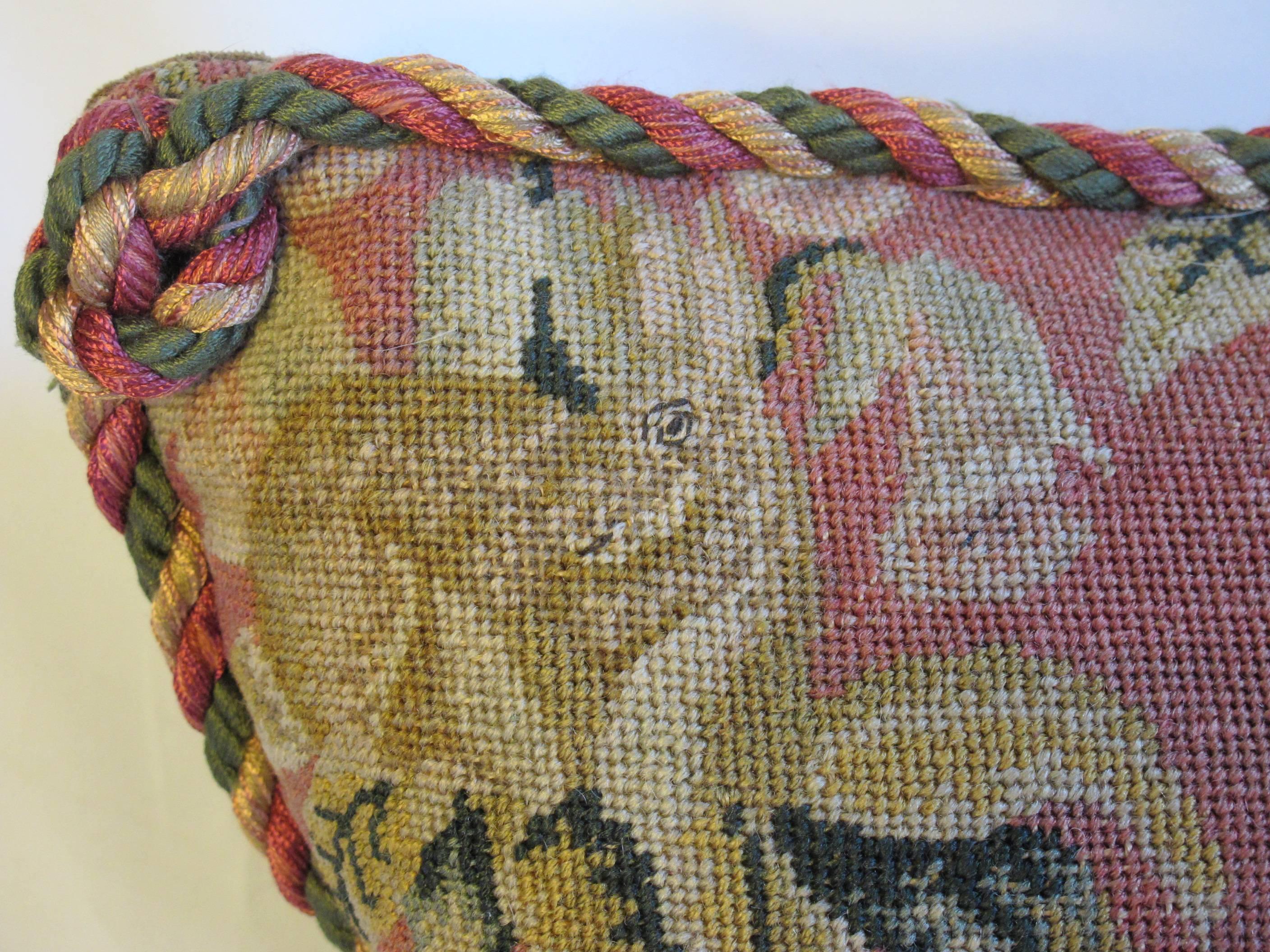 A pillow made from an early 20th century needlepoint depicting a charming woodland scene with foliage and small animals, embellished with hand-knotted cord trim, hidden zipper closure, down insert is included.