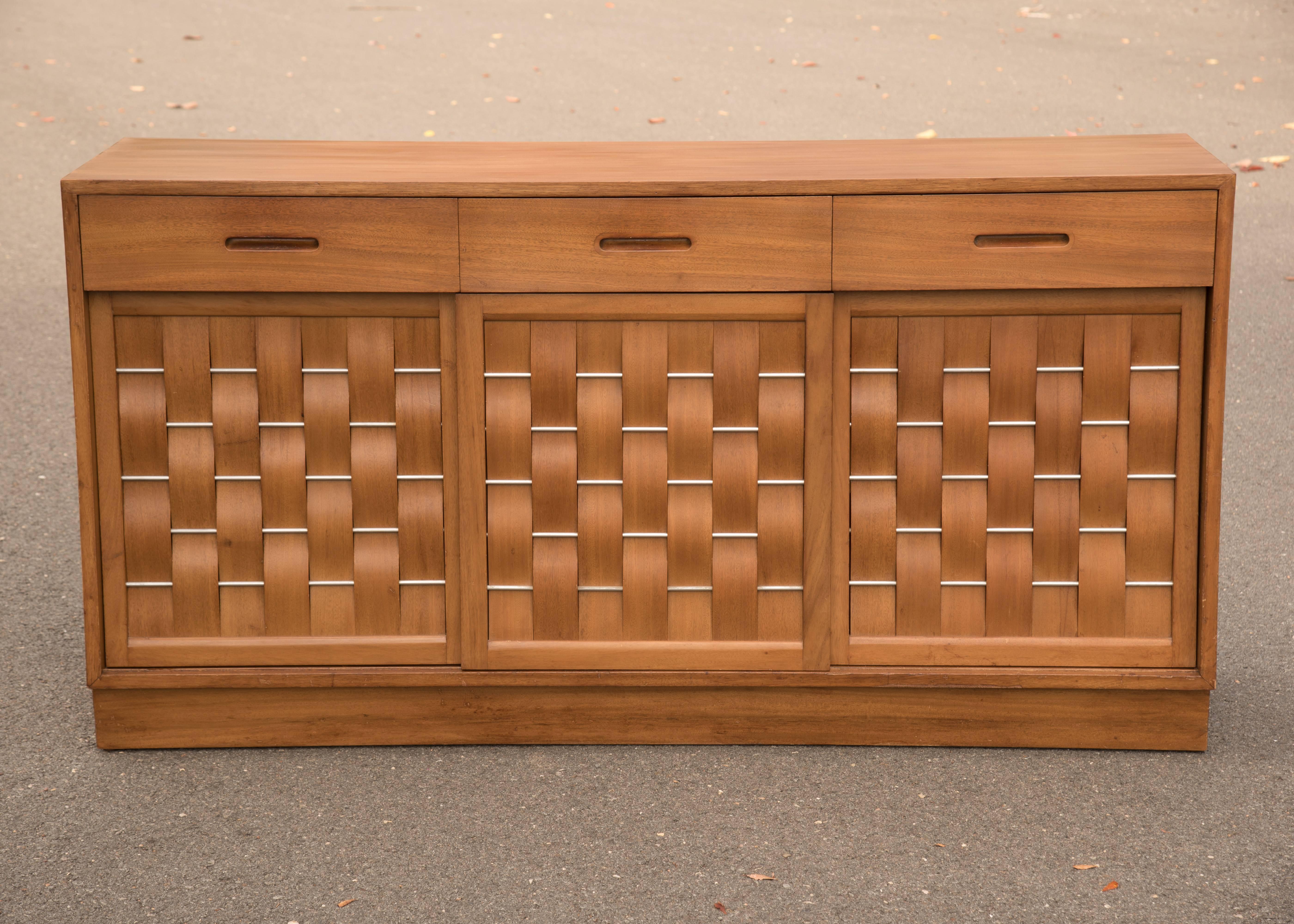 Stunning Mid-Century Modern cabinet by Edward Wormley for Dunbar having 
woven front panel doors that slide open to reveal three drawers on the right and left and shelves in the center. Mahogany, aluminum; marked on back.
  