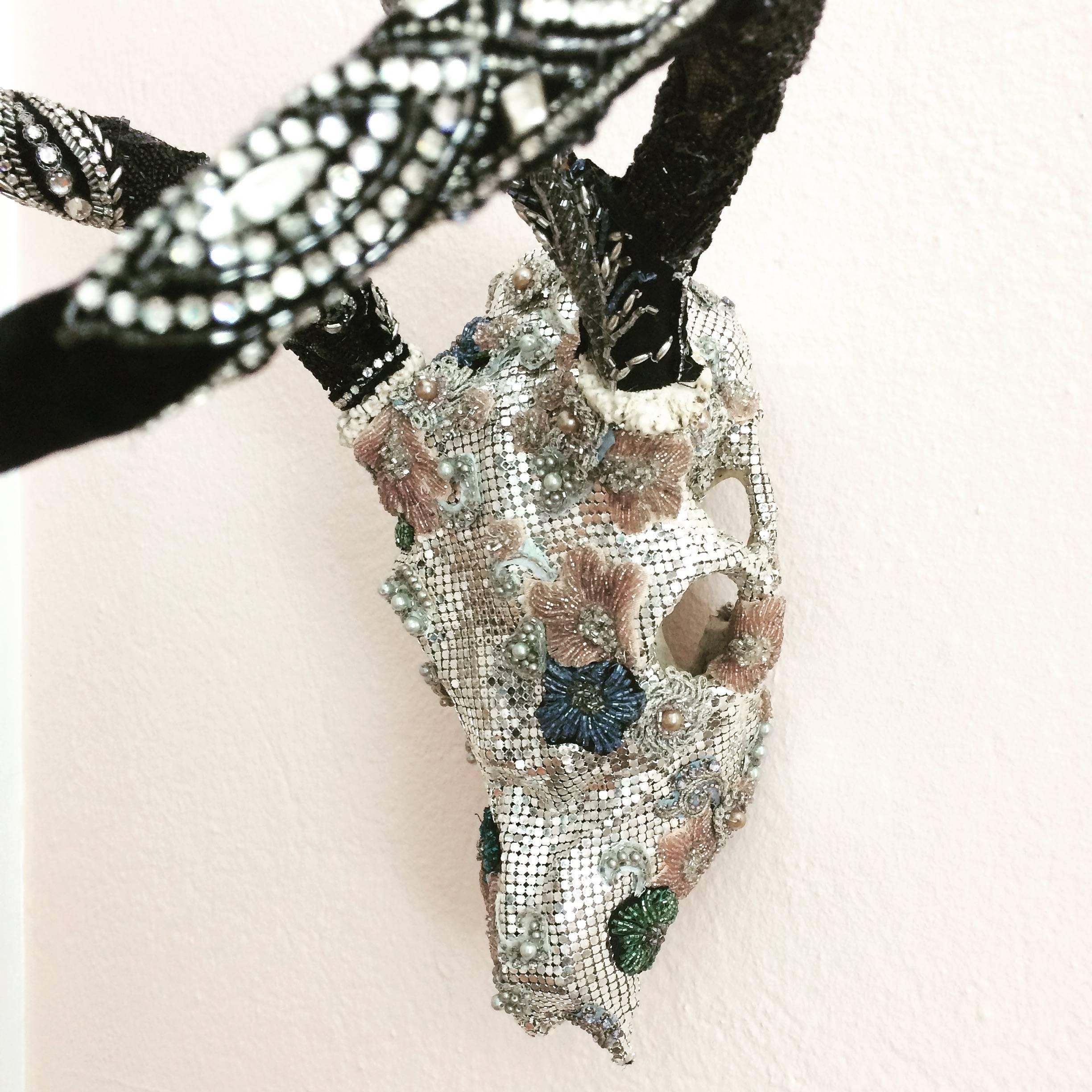 One of a kind mixed media jewel of a wall sculpture made from a small skull, meticulously adorned with vintage pieces of beaded fabrics, lace and a silver mesh evening bag.

By Fay Sciarra.